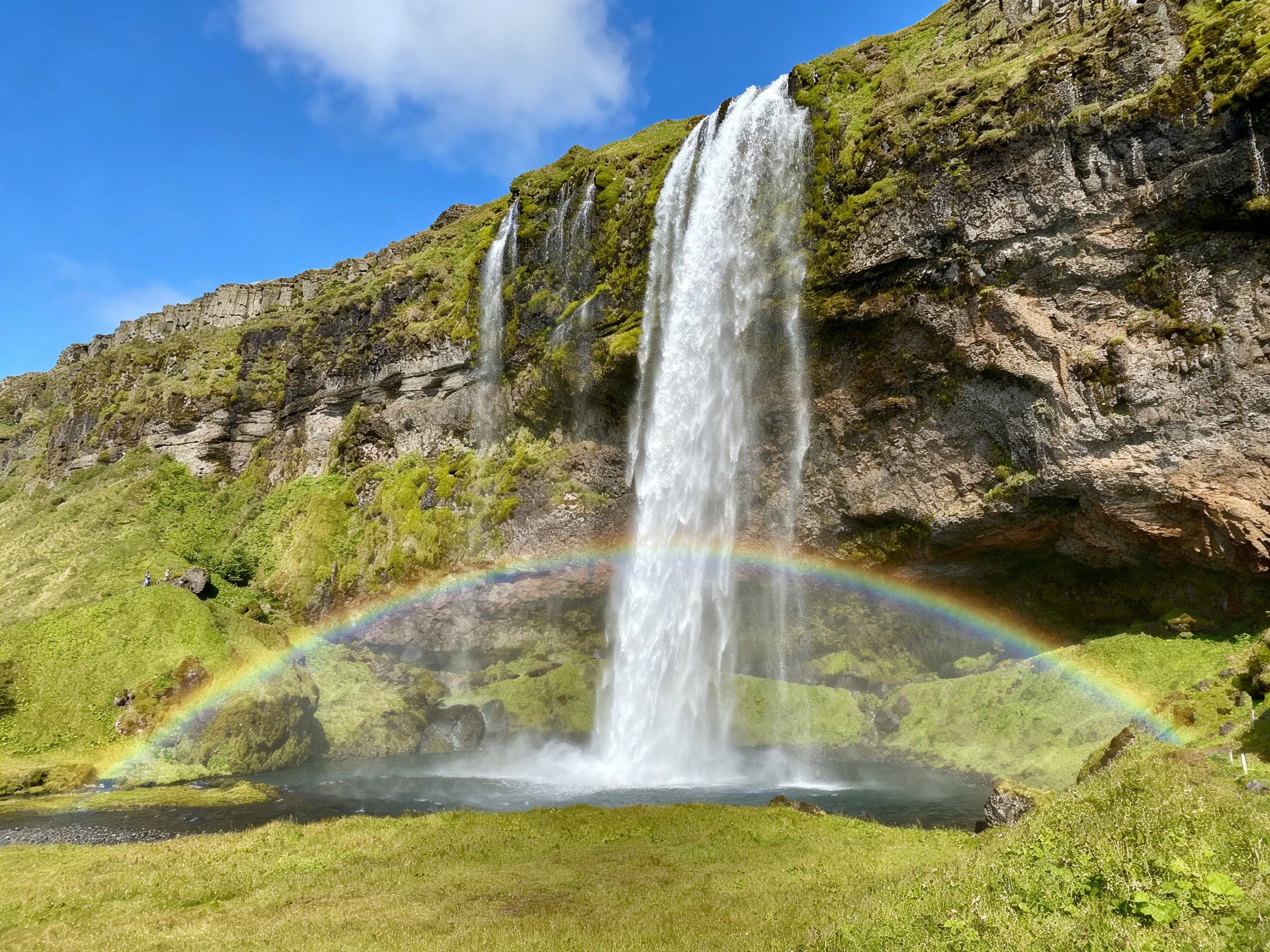A majestic waterfall cascades over mossy cliffs with a vibrant rainbow below