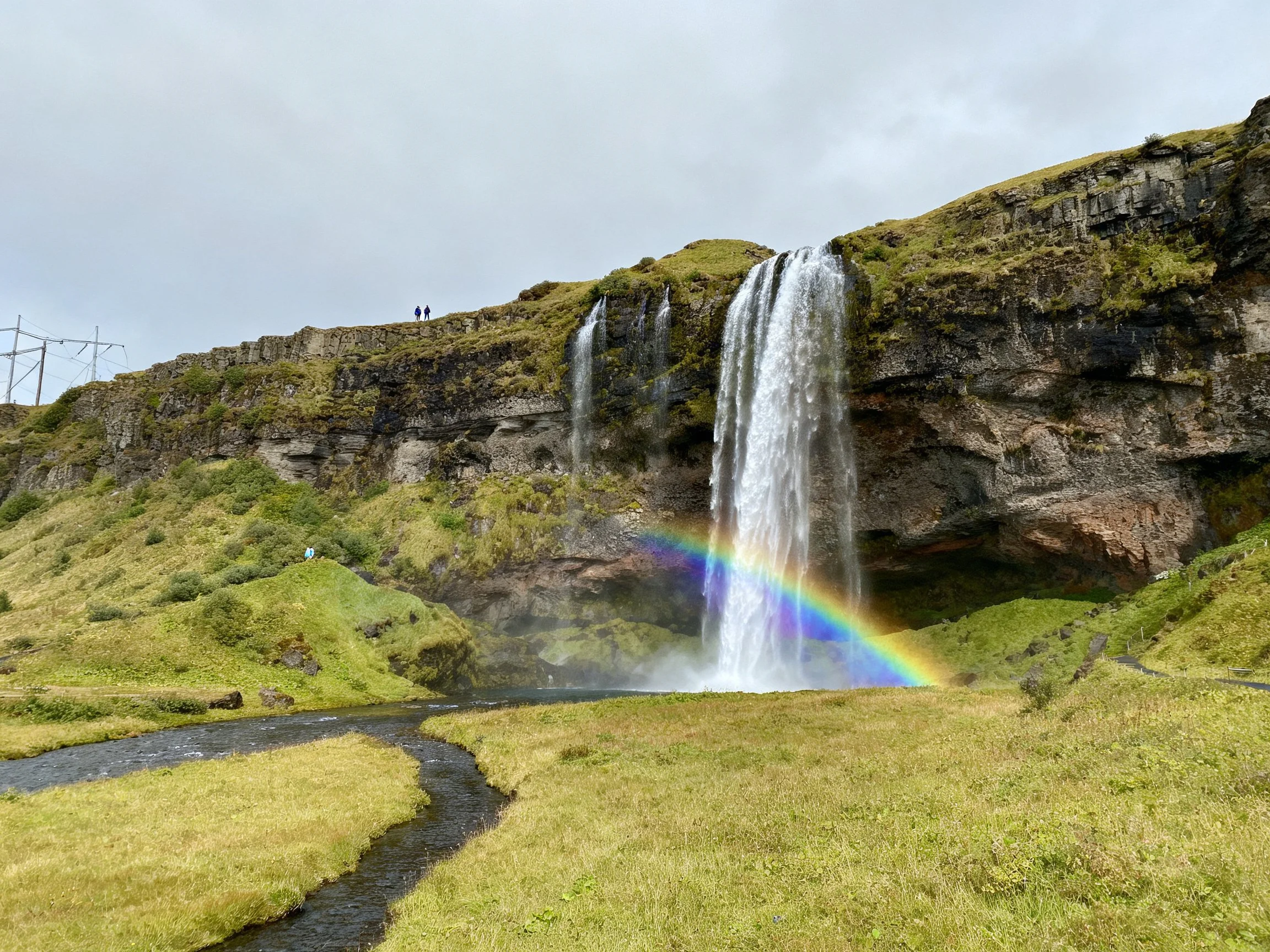 A majestic waterfall cascades over rocky cliffs with a vibrant rainbow below