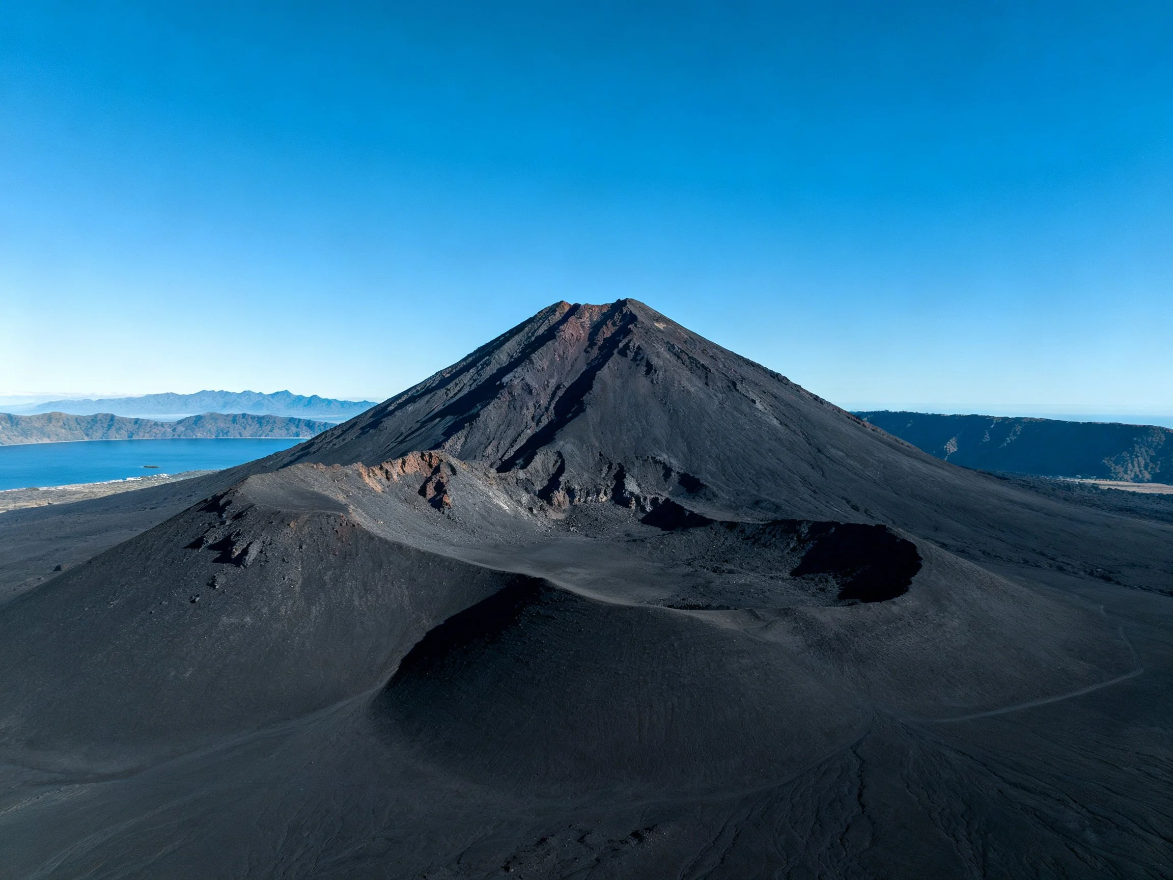A massive black volcanic peak under a clear blue sky