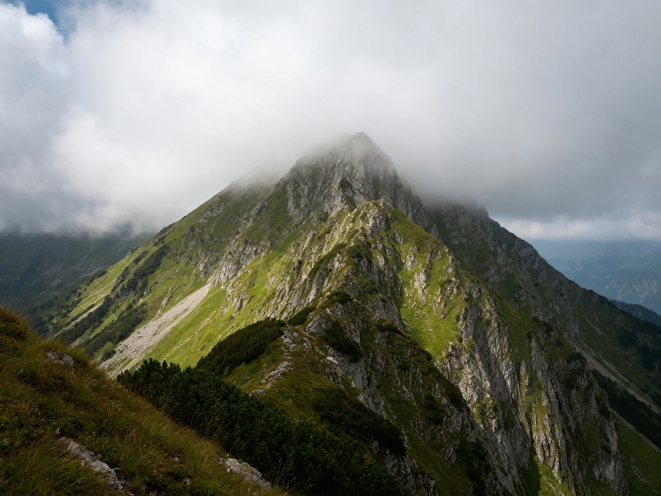 A mist-shrouded mountain peak with green slopes and rocky terrain