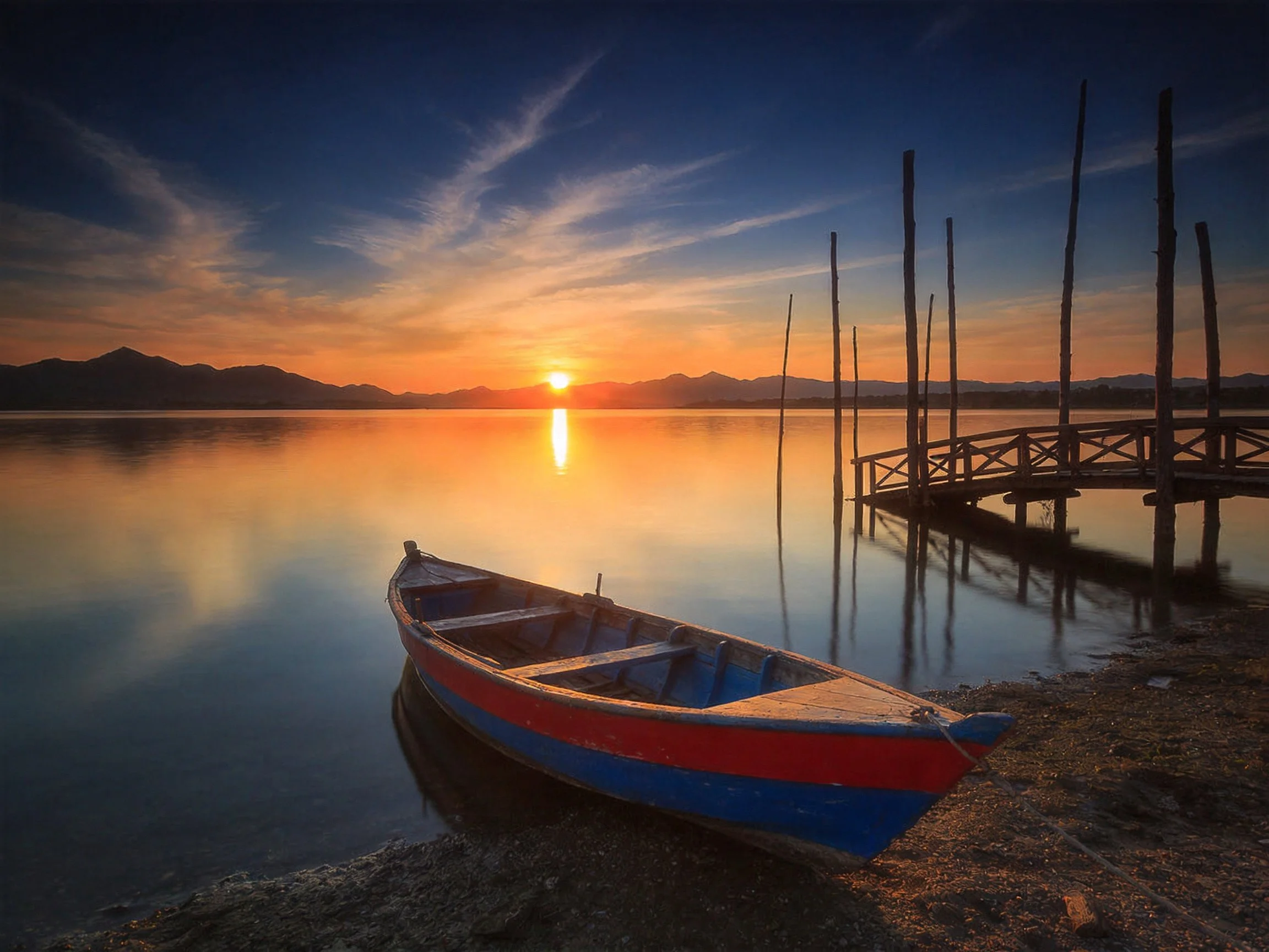 A red and blue boat near a wooden dock at sunset