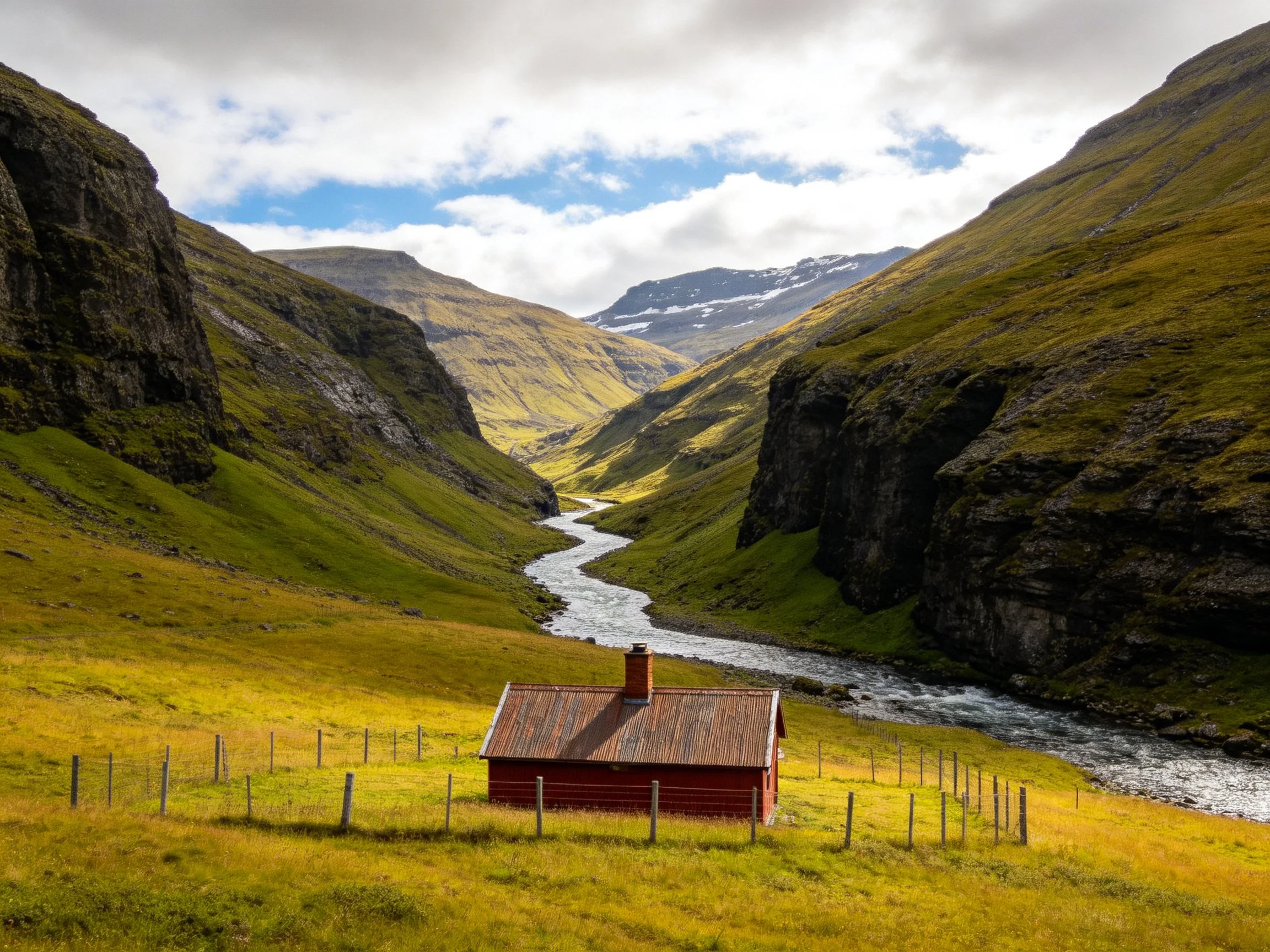 A red wooden cabin near a winding river in a green mountain valley