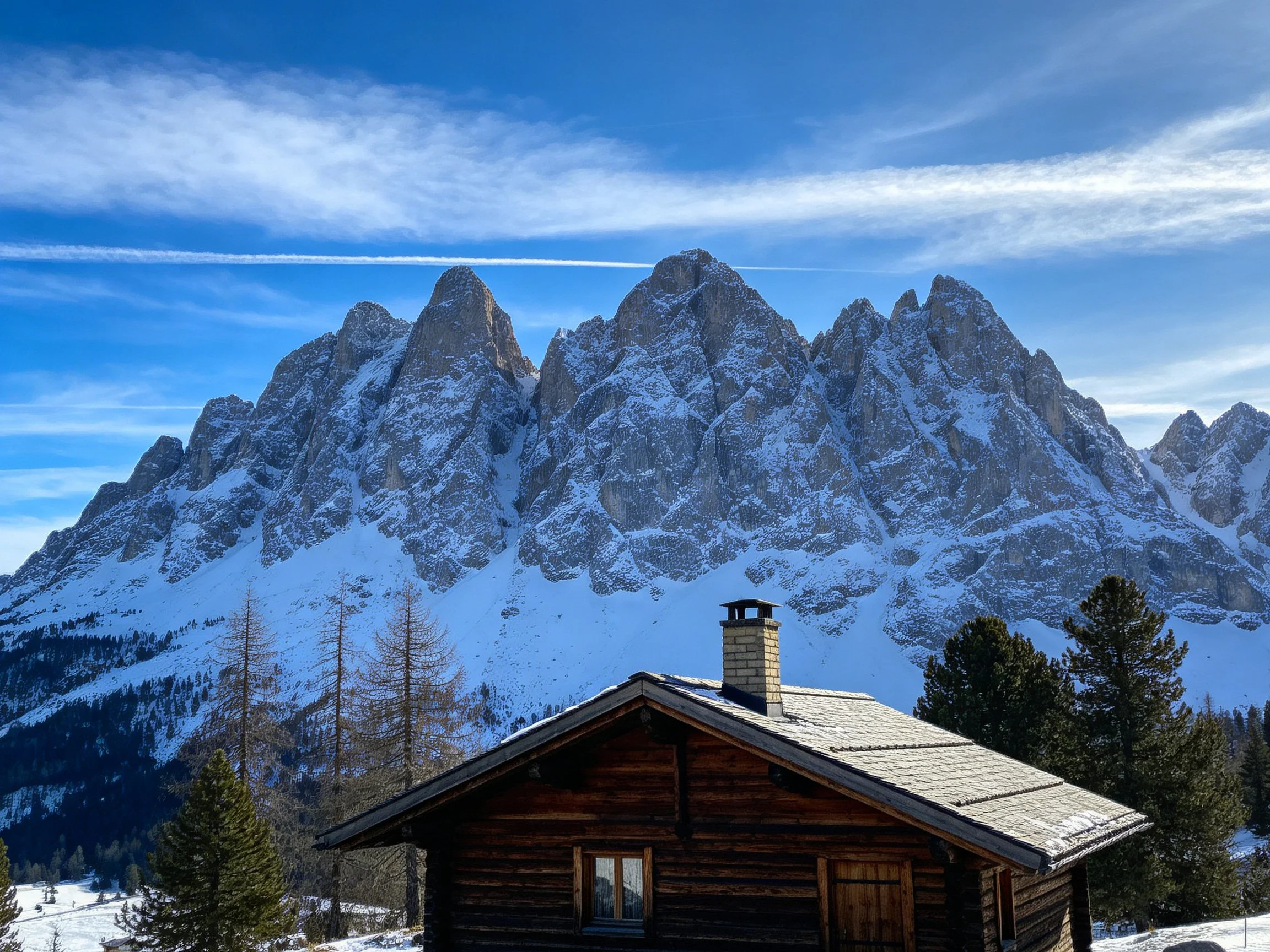 A rustic wooden cabin beside snow-capped mountain peaks