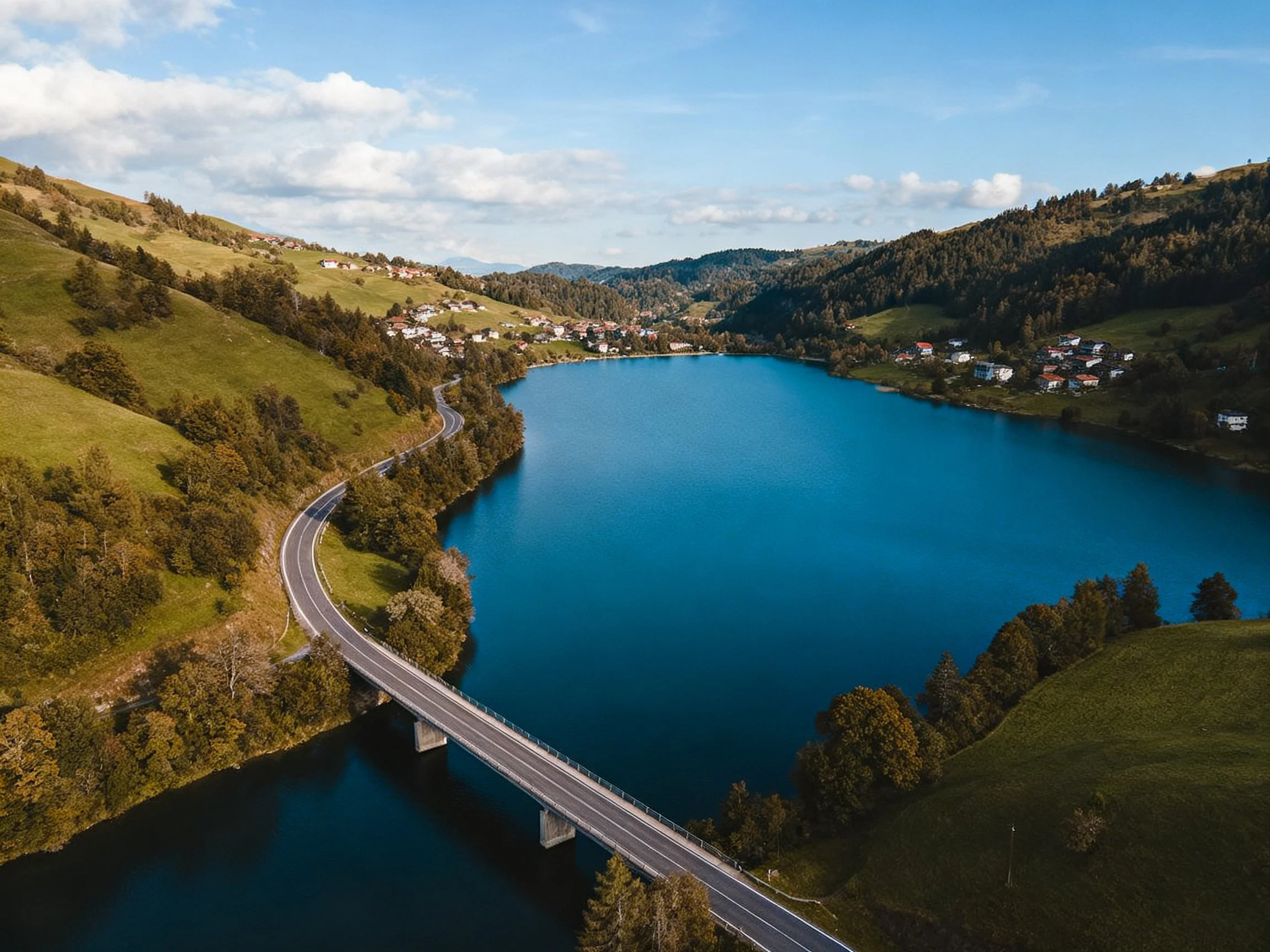 A scenic landscape with a large blue lake, bridge, and hillside village.