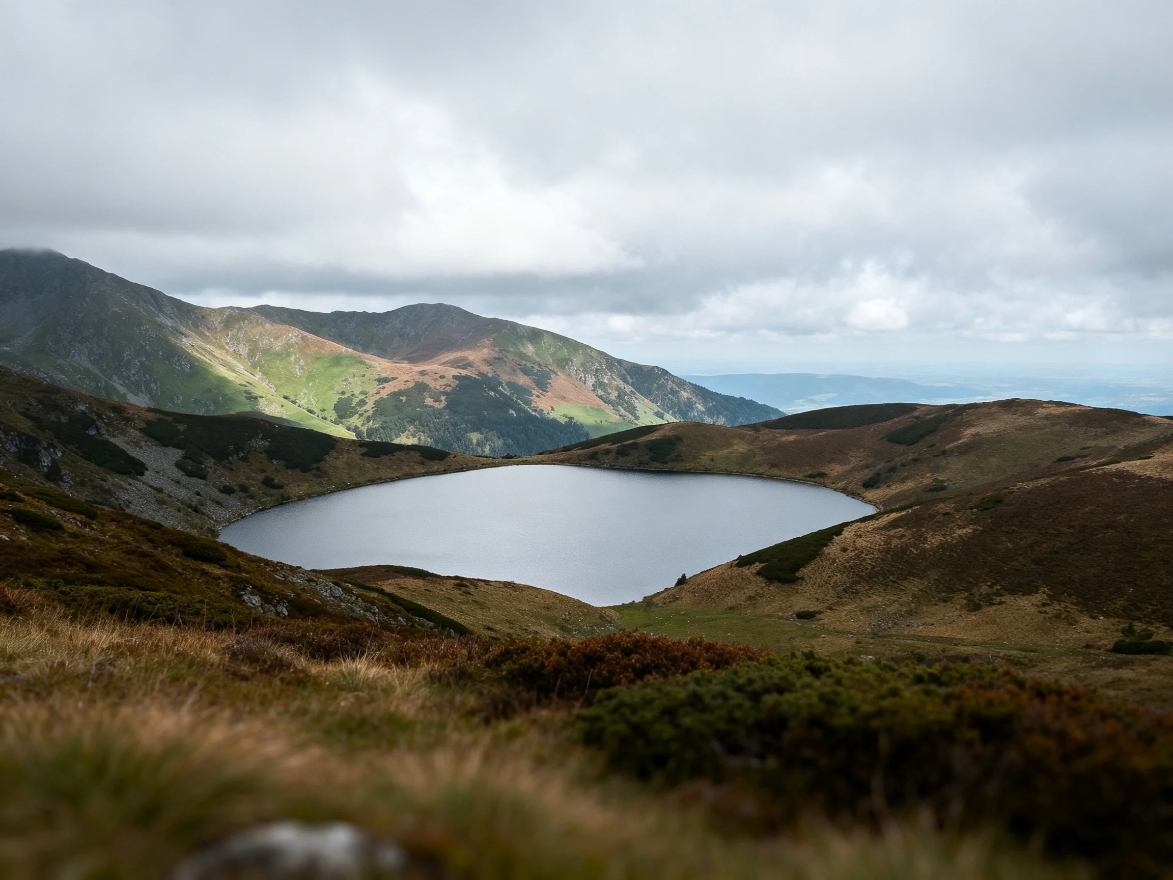 A serene alpine lake surrounded by rolling brown and green mountains
