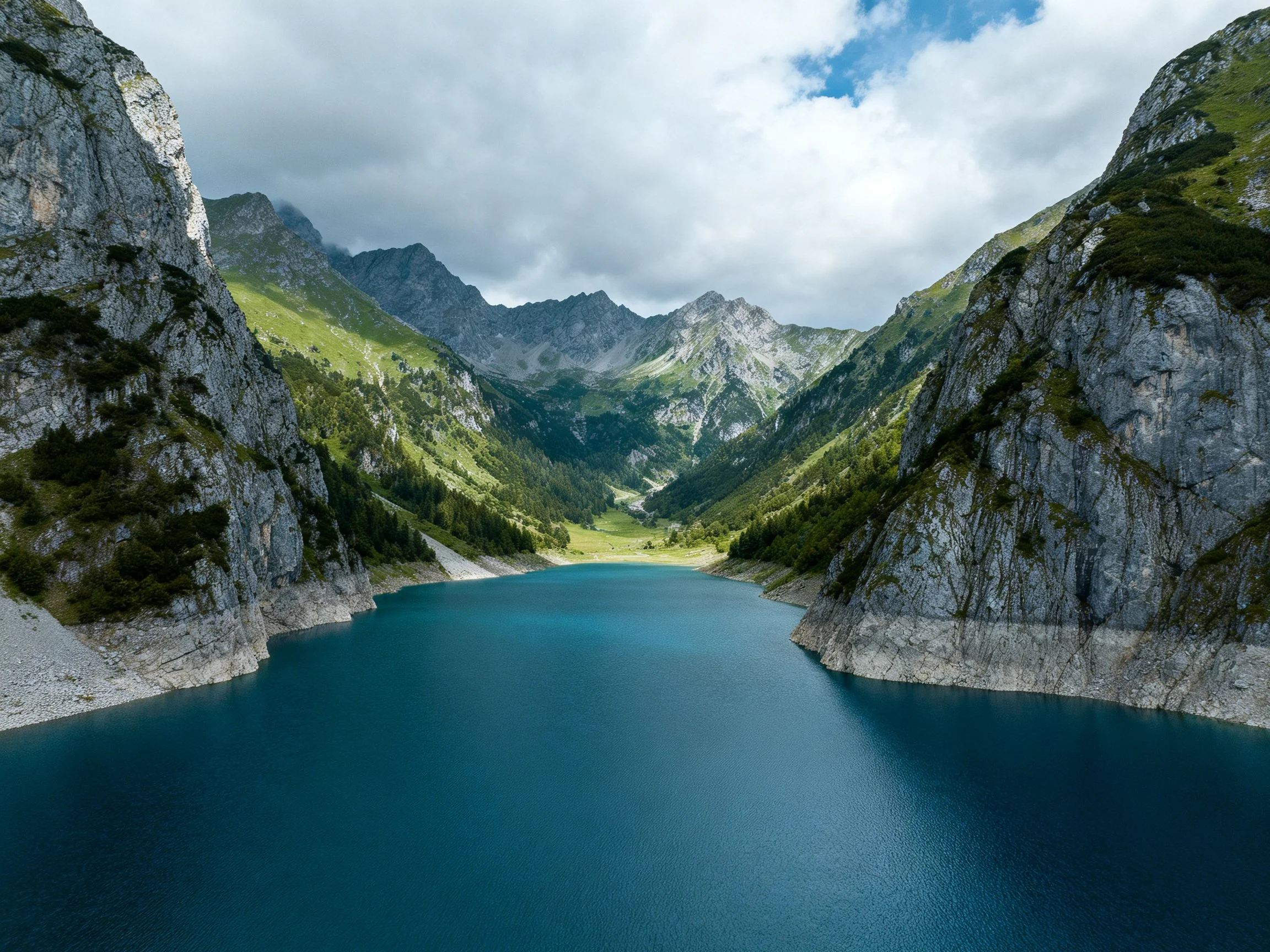 A serene alpine lake surrounded by rugged gray cliffs and lush green slopes