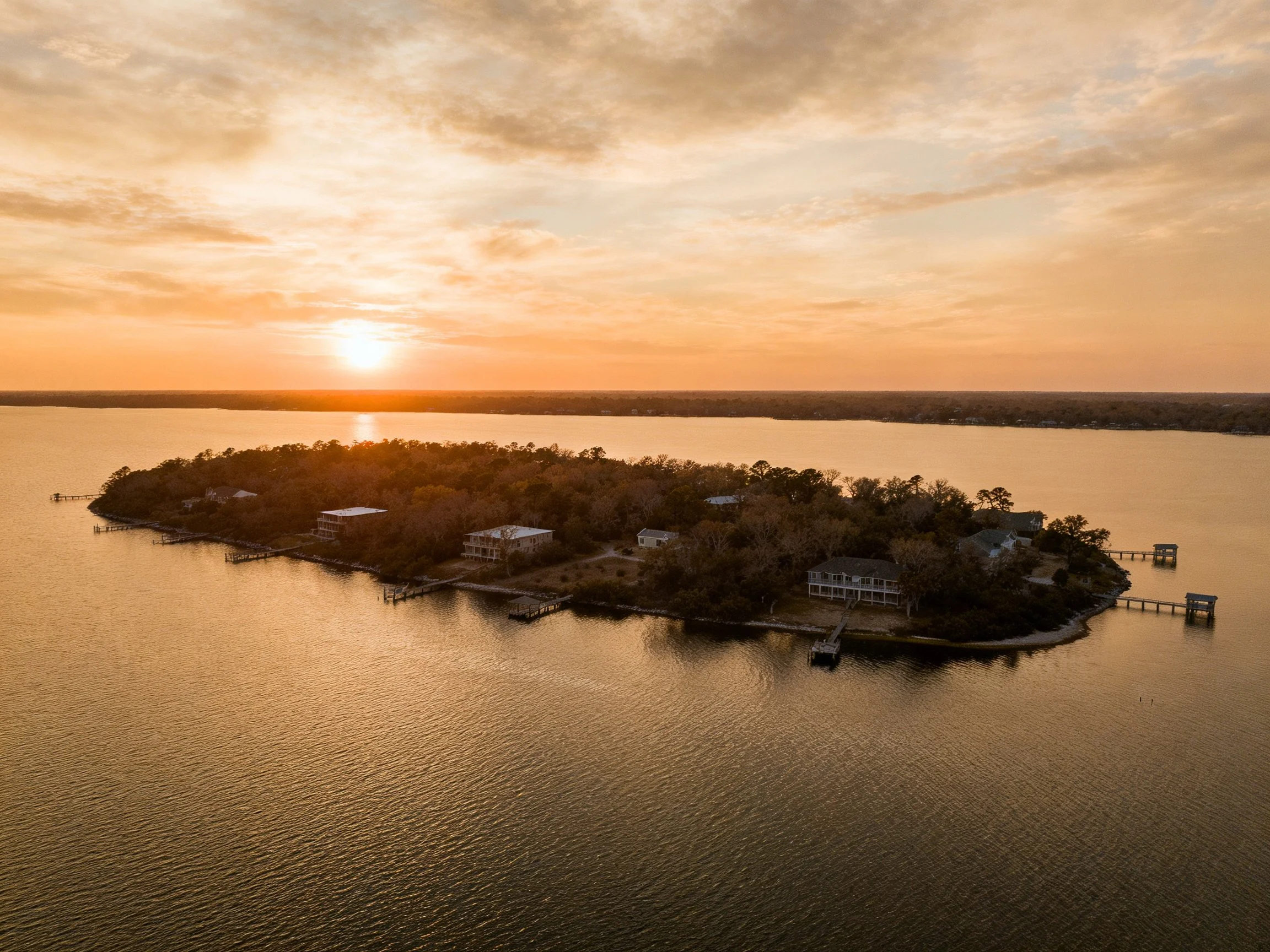 A serene island with homes, calm waters, and golden sunset