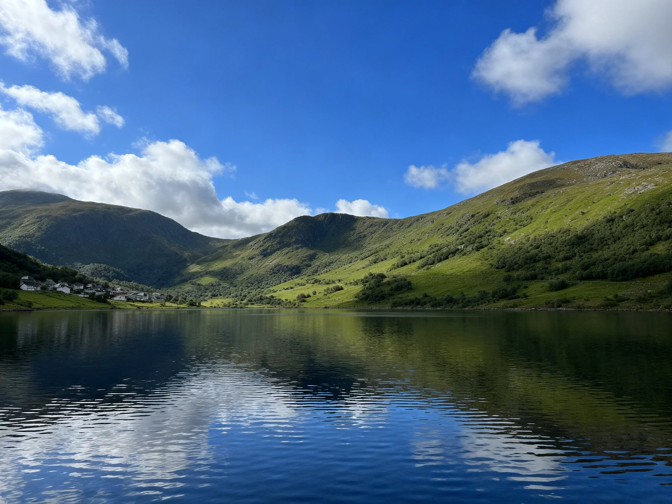 A serene lake surrounded by lush green mountains under bright blue skies