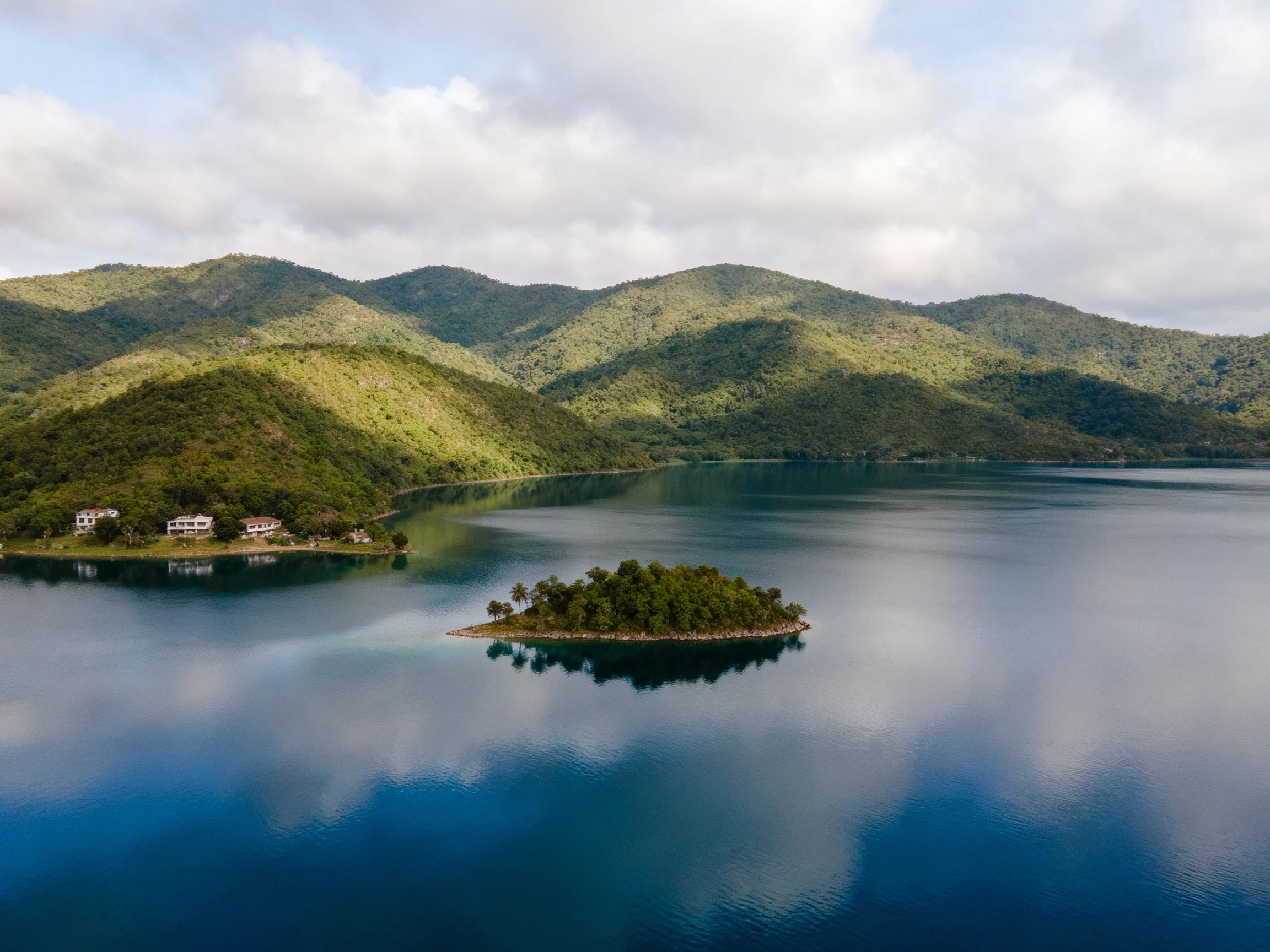 A serene lake with lush green hills, a small island, and shoreline homes