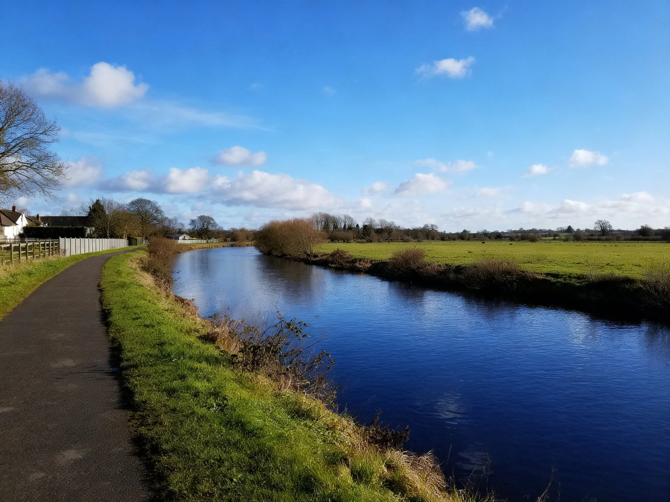 A serene river with a paved path, lush greenery, and clear blue sky