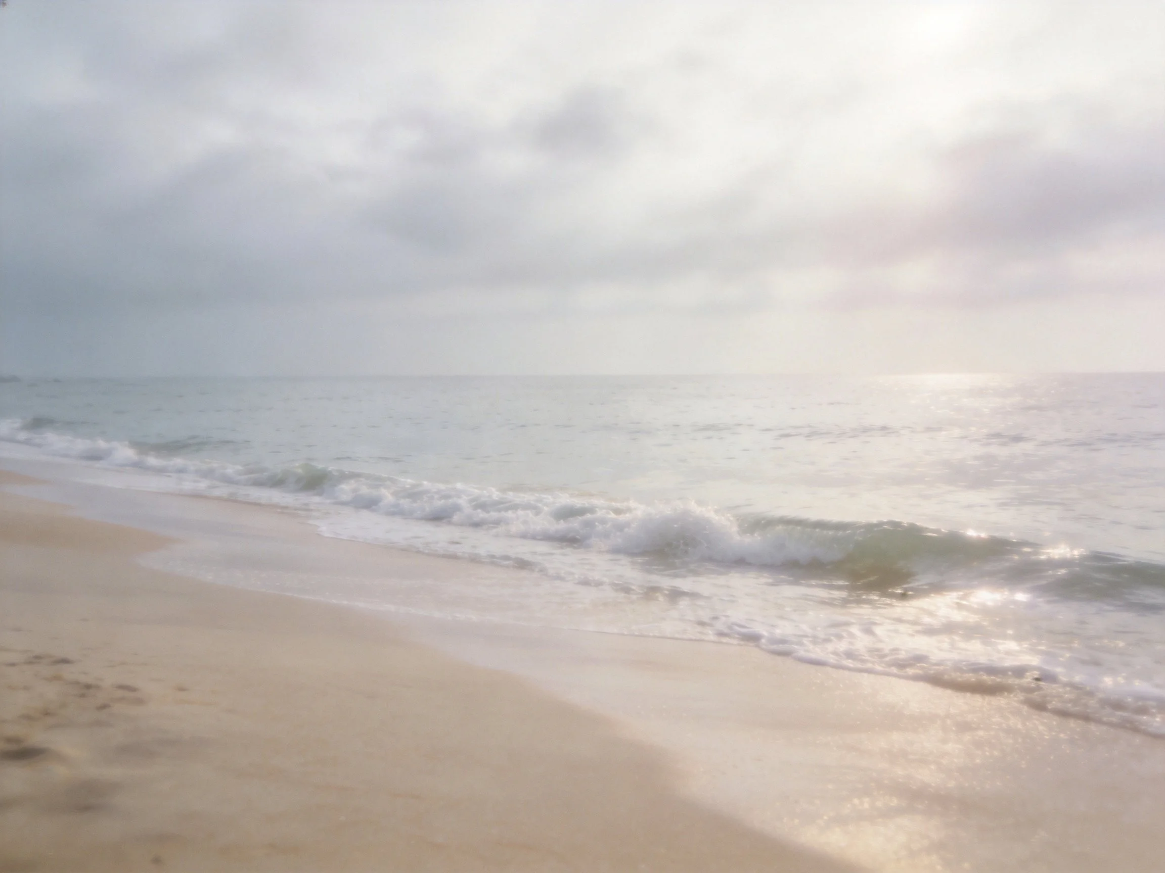 A serene sandy beach with gentle ocean waves under cloudy skies