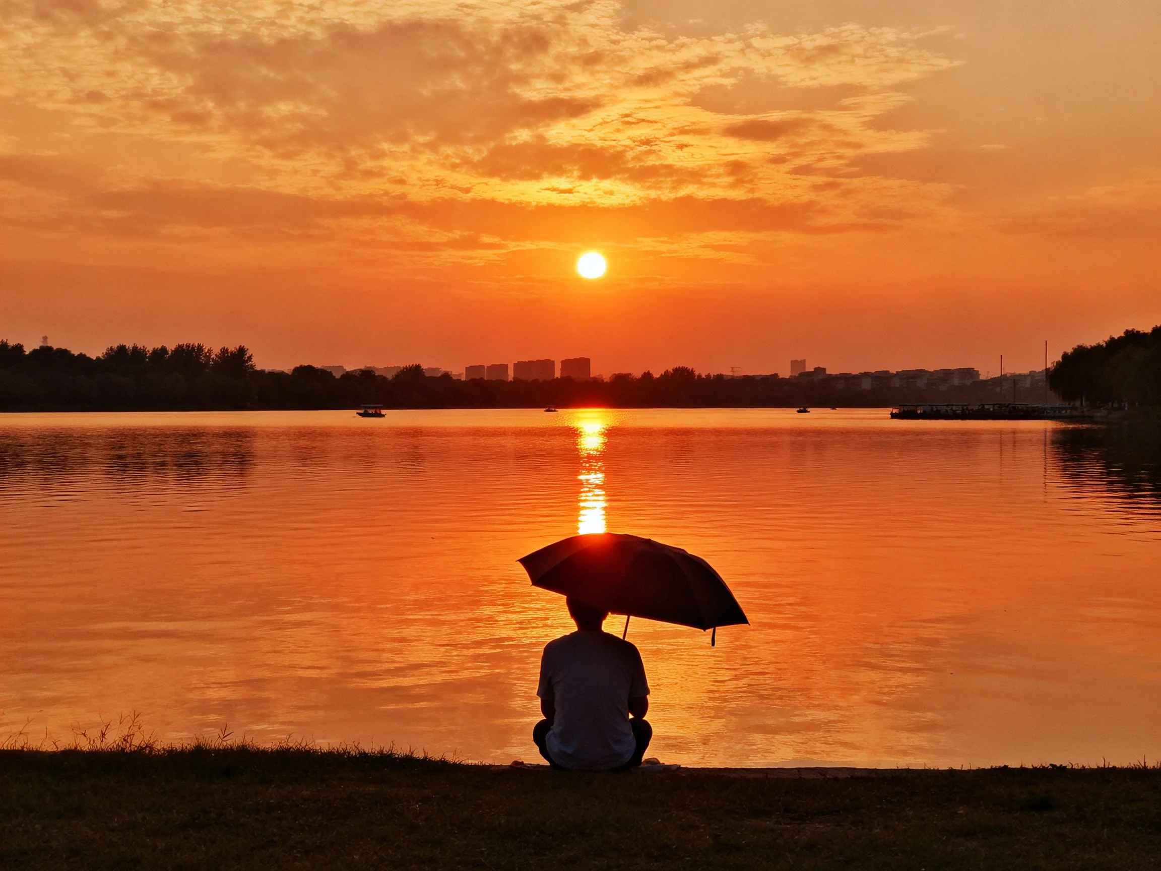 A silhouetted figure with umbrella by a reflective lake during a vibrant sunset