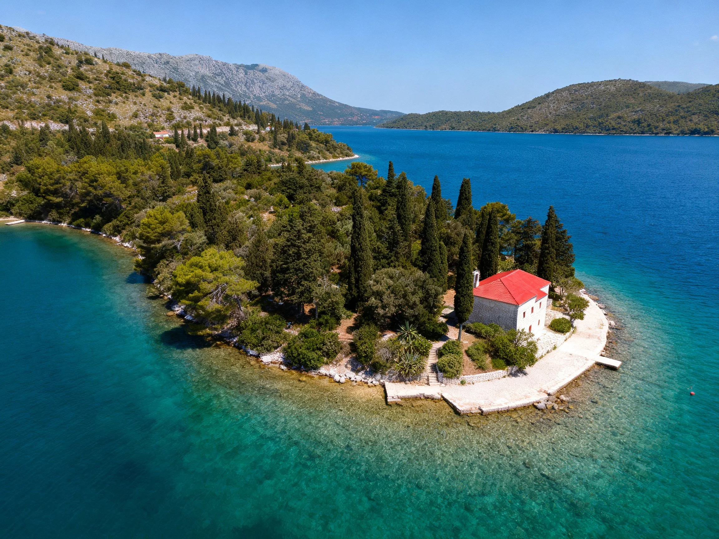 A small island with a white house, red roof, and turquoise waters