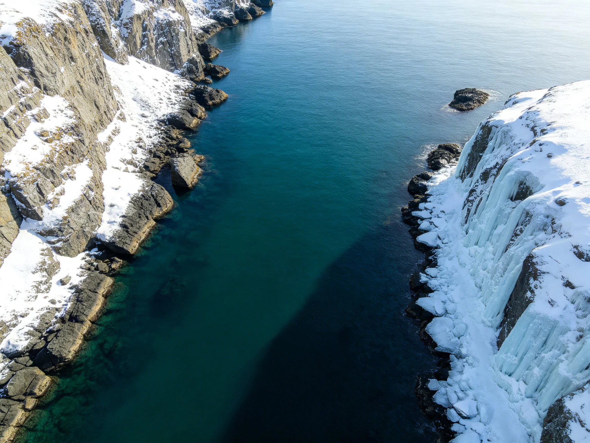 A snowy cliffside coastline with icy waterfalls and deep blue waters