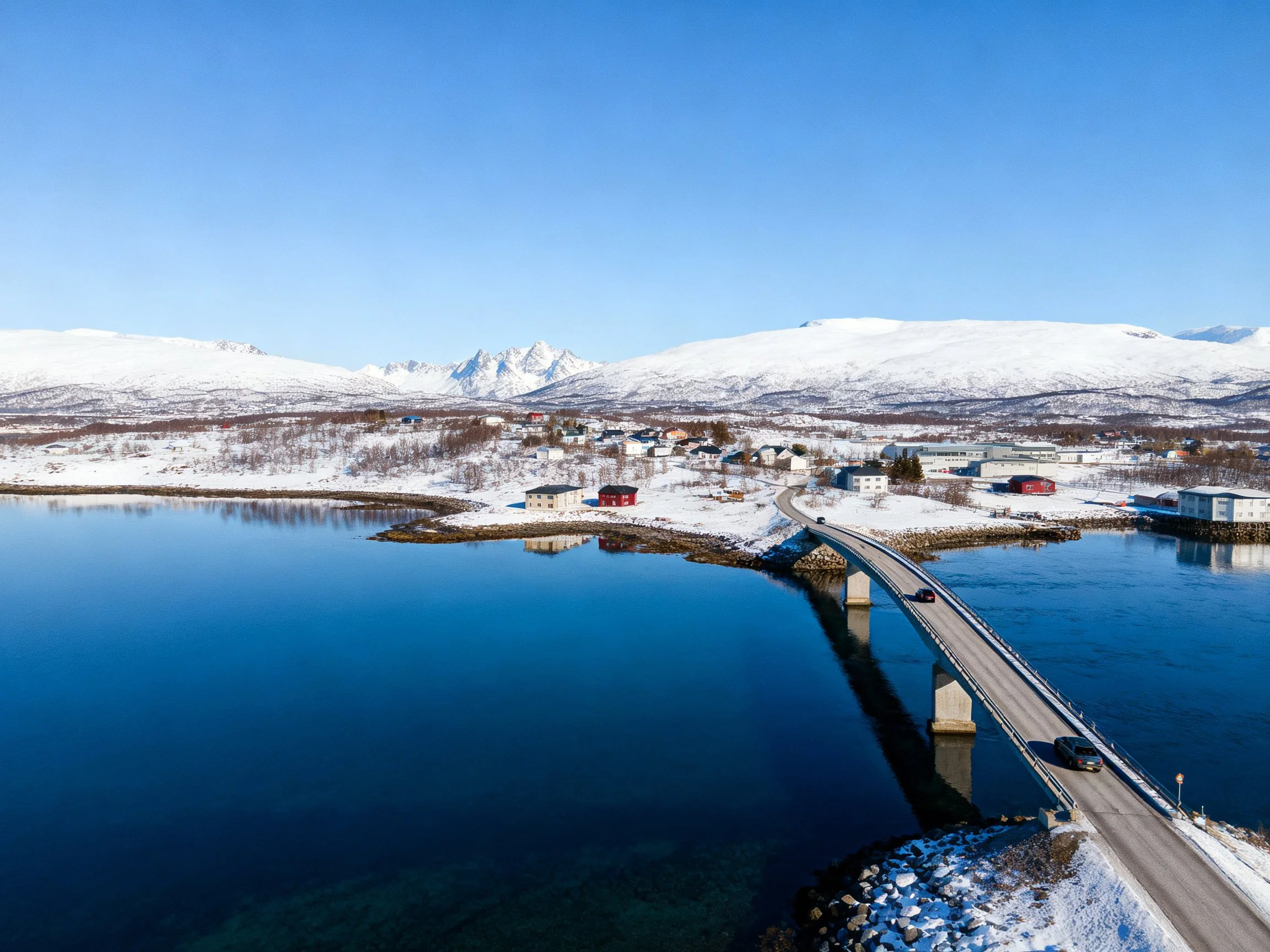 A snowy mountain village connected by a bridge over clear blue waters