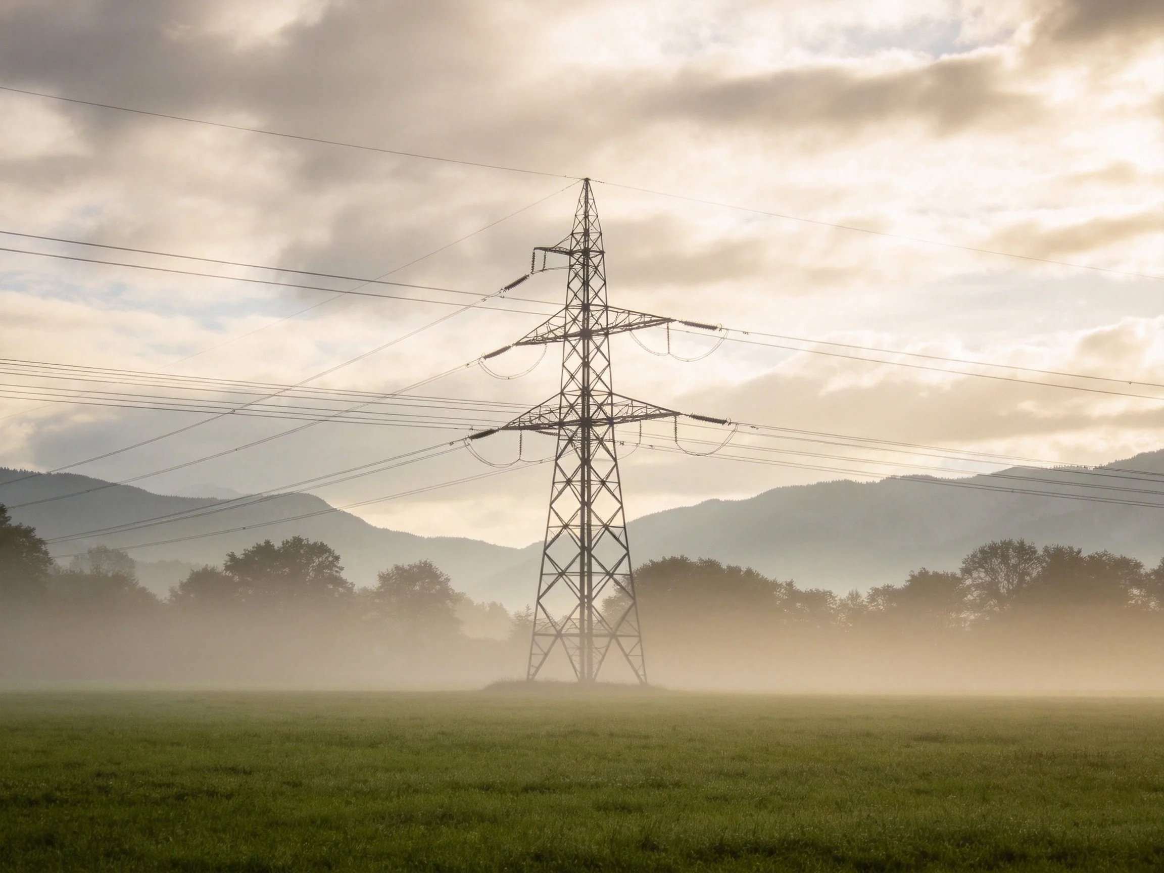 A tall metal power tower in a misty green field near mountains