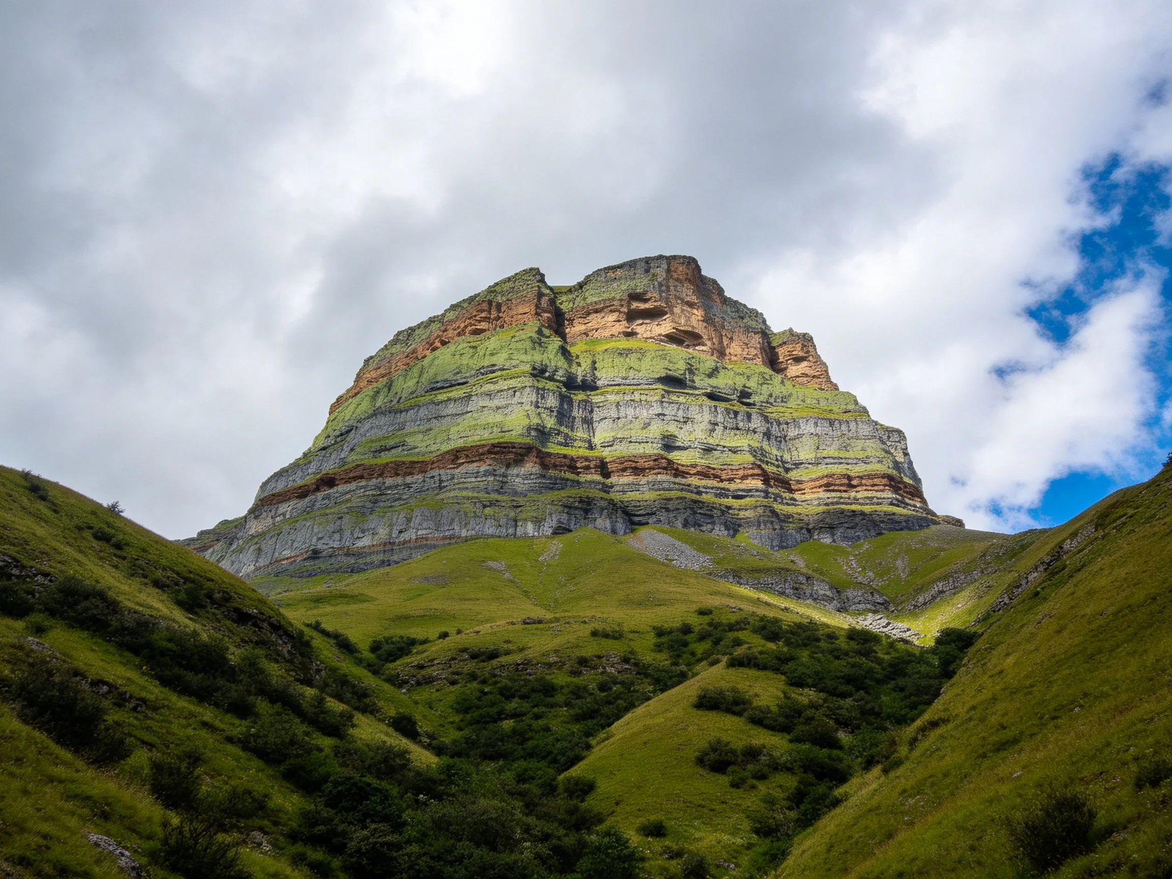 A towering multicolored cliff with lush green slopes