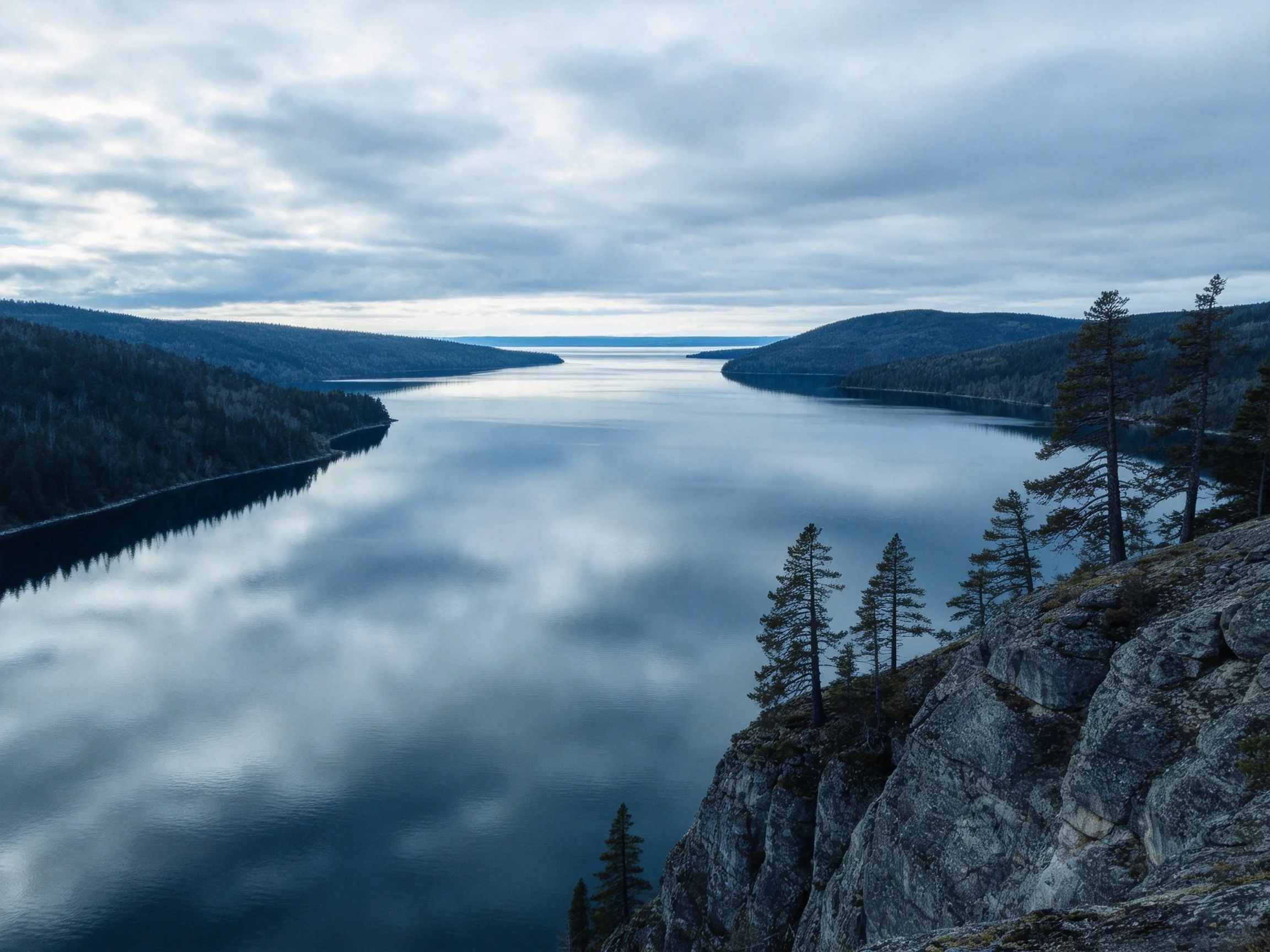 A tranquil lake reflects overcast skies near forested hills