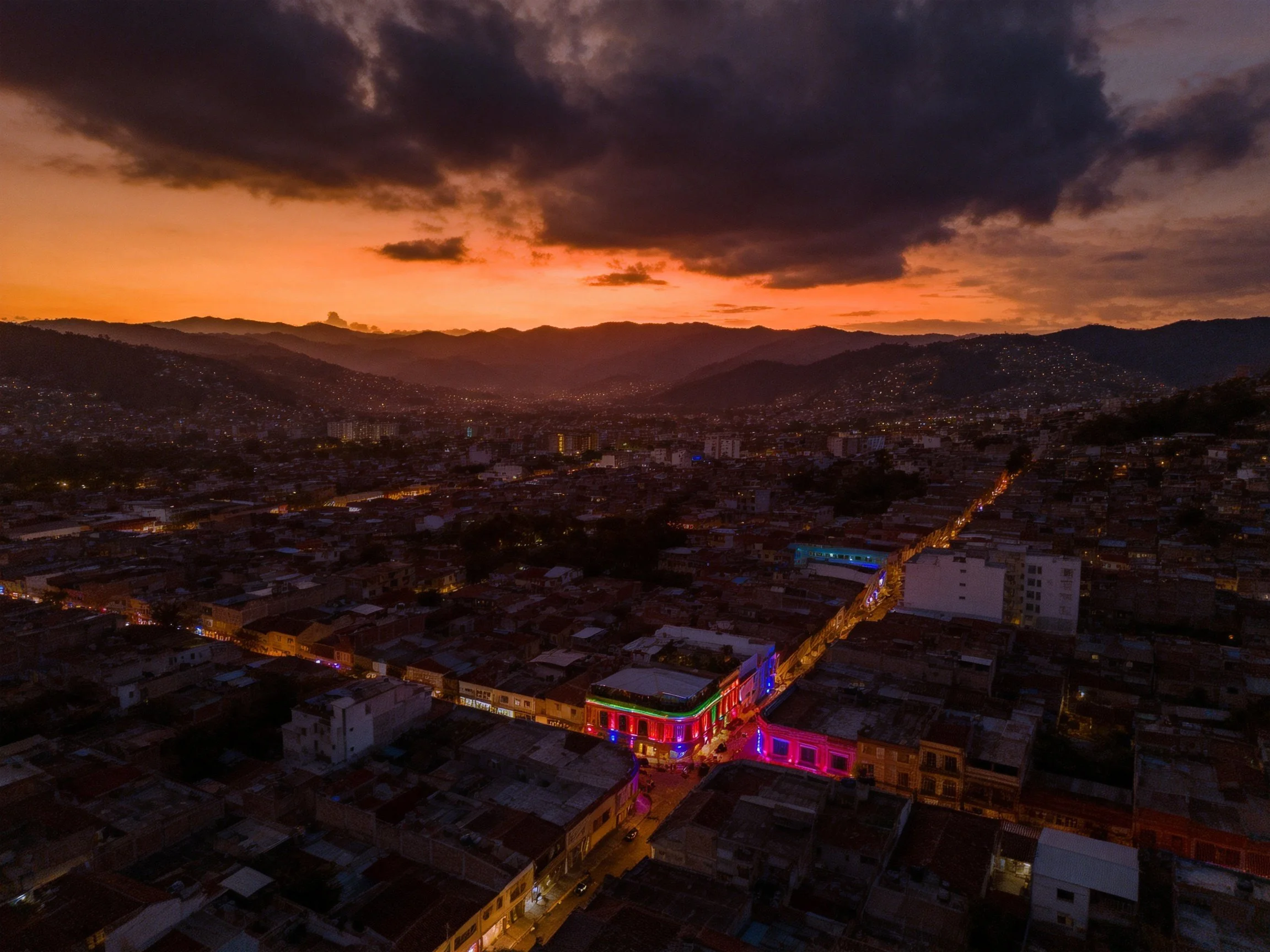 A vibrant cityscape at dusk with colorful buildings and mountain backdrop