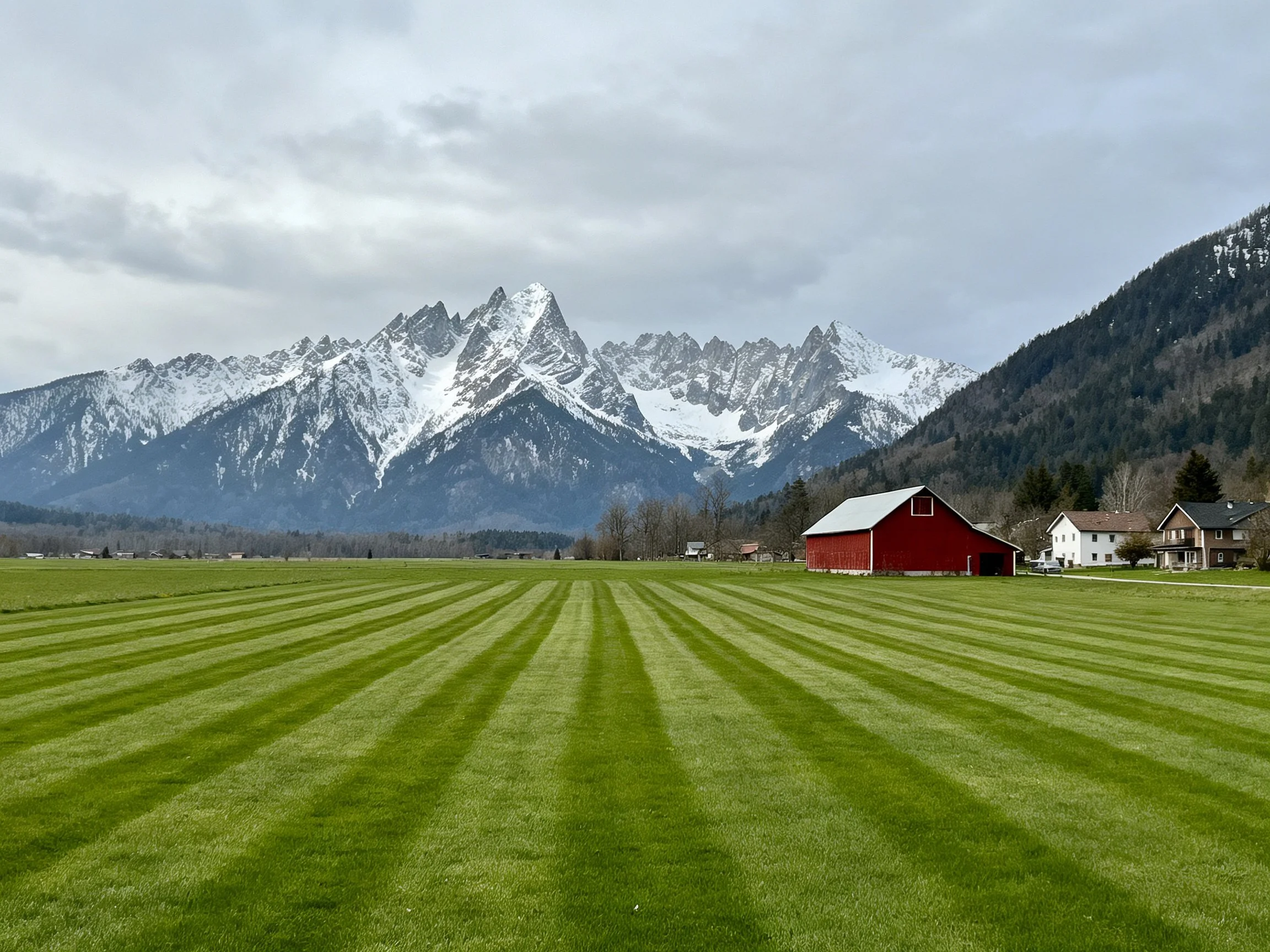 A vibrant green field with a red barn near snow-capped mountains