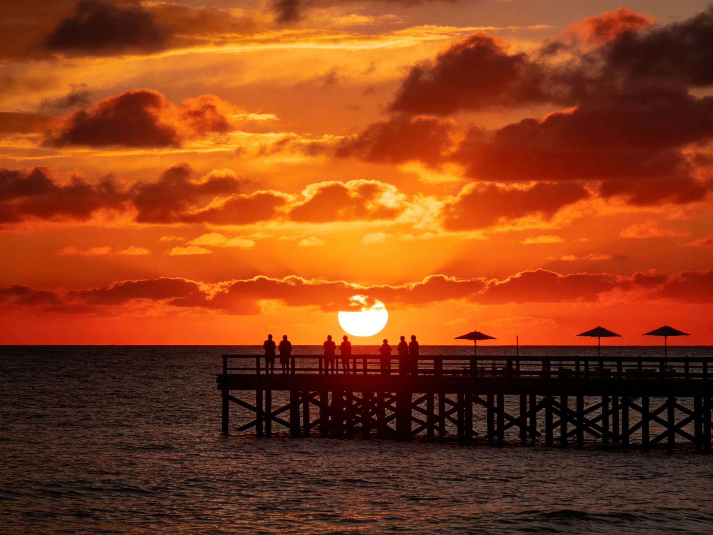 A vibrant orange sunset over a wooden pier with silhouetted figures