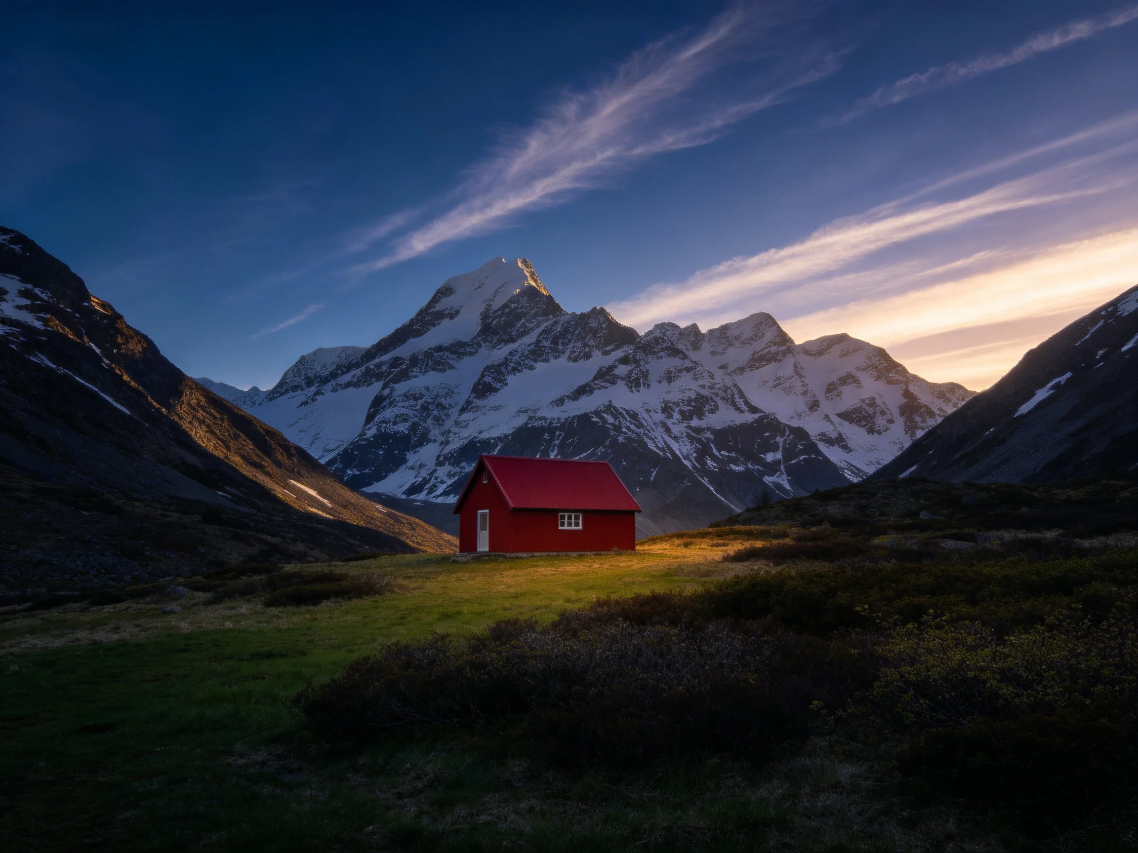 A vibrant red cabin near snow-capped peaks under twilight skies