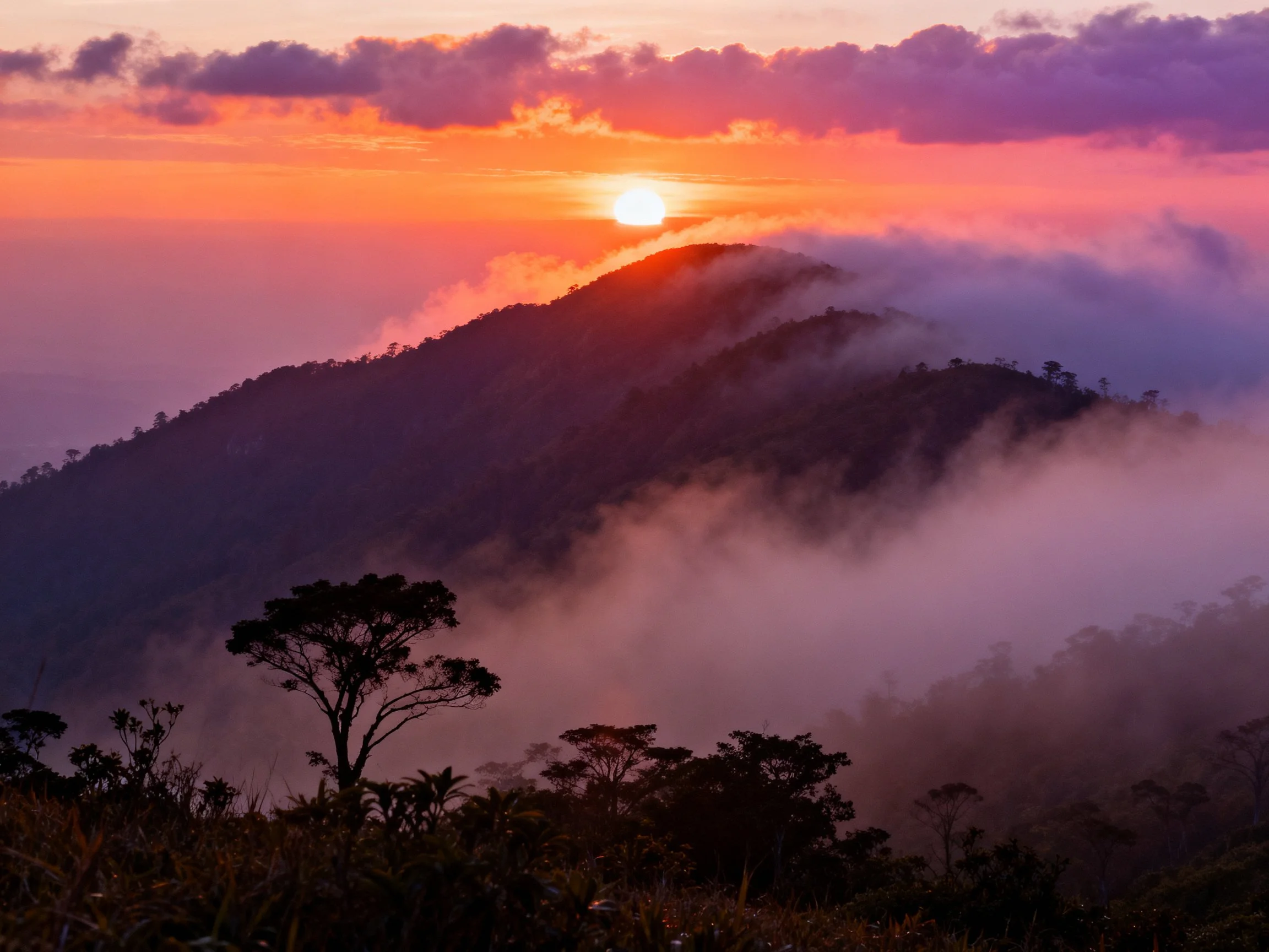 A vibrant sunset illuminates mist-covered mountain peaks