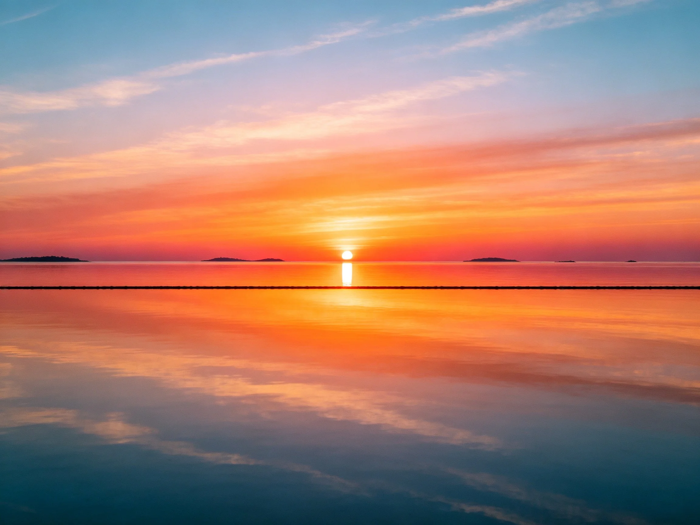 A vibrant sunset over calm water with orange sky reflections