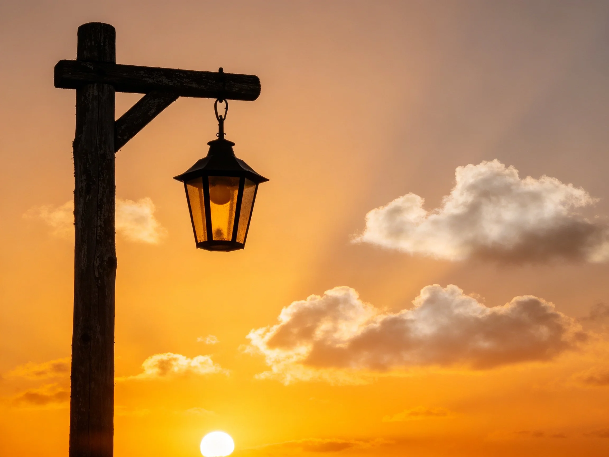 A vintage wooden streetlamp silhouetted by golden sunset skies