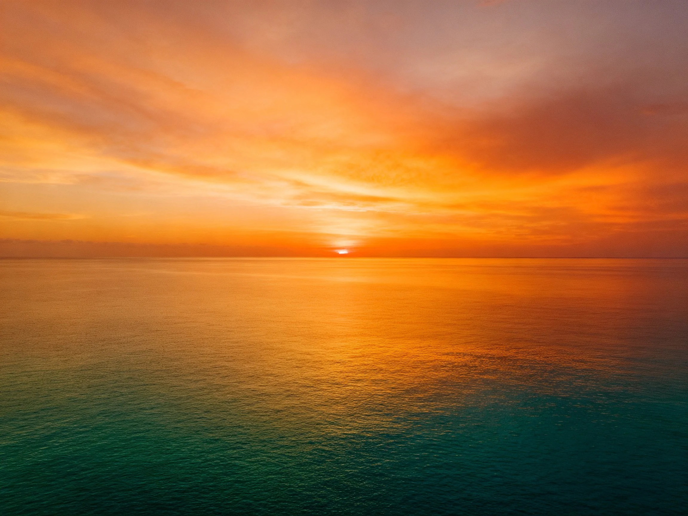 A vivid orange sunset illuminates calm turquoise waters