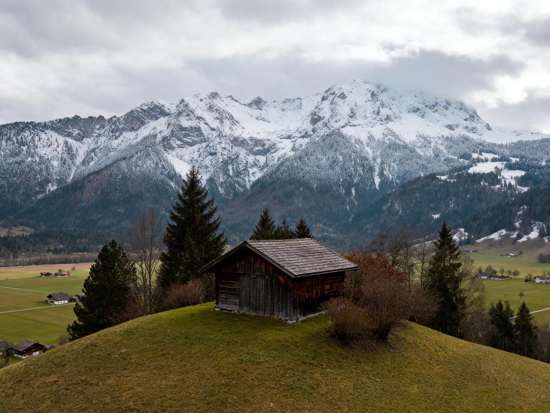 A weathered wooden cabin near snow-capped mountain peaks