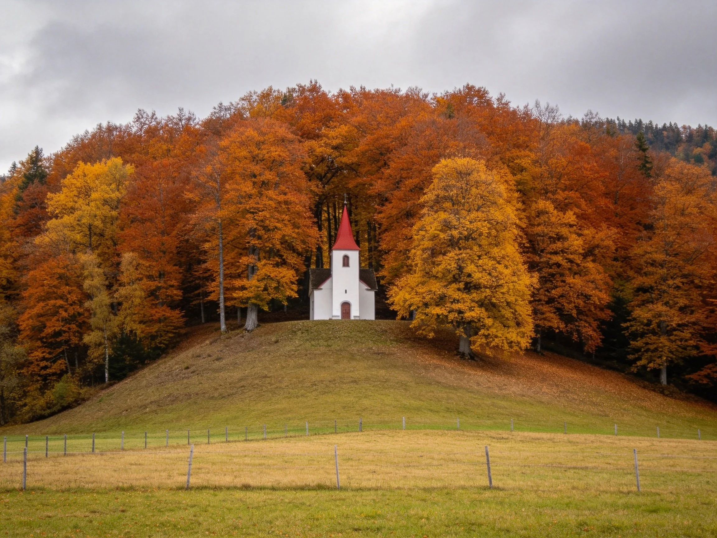 A white chapel atop a hill amidst autumn-hued forests