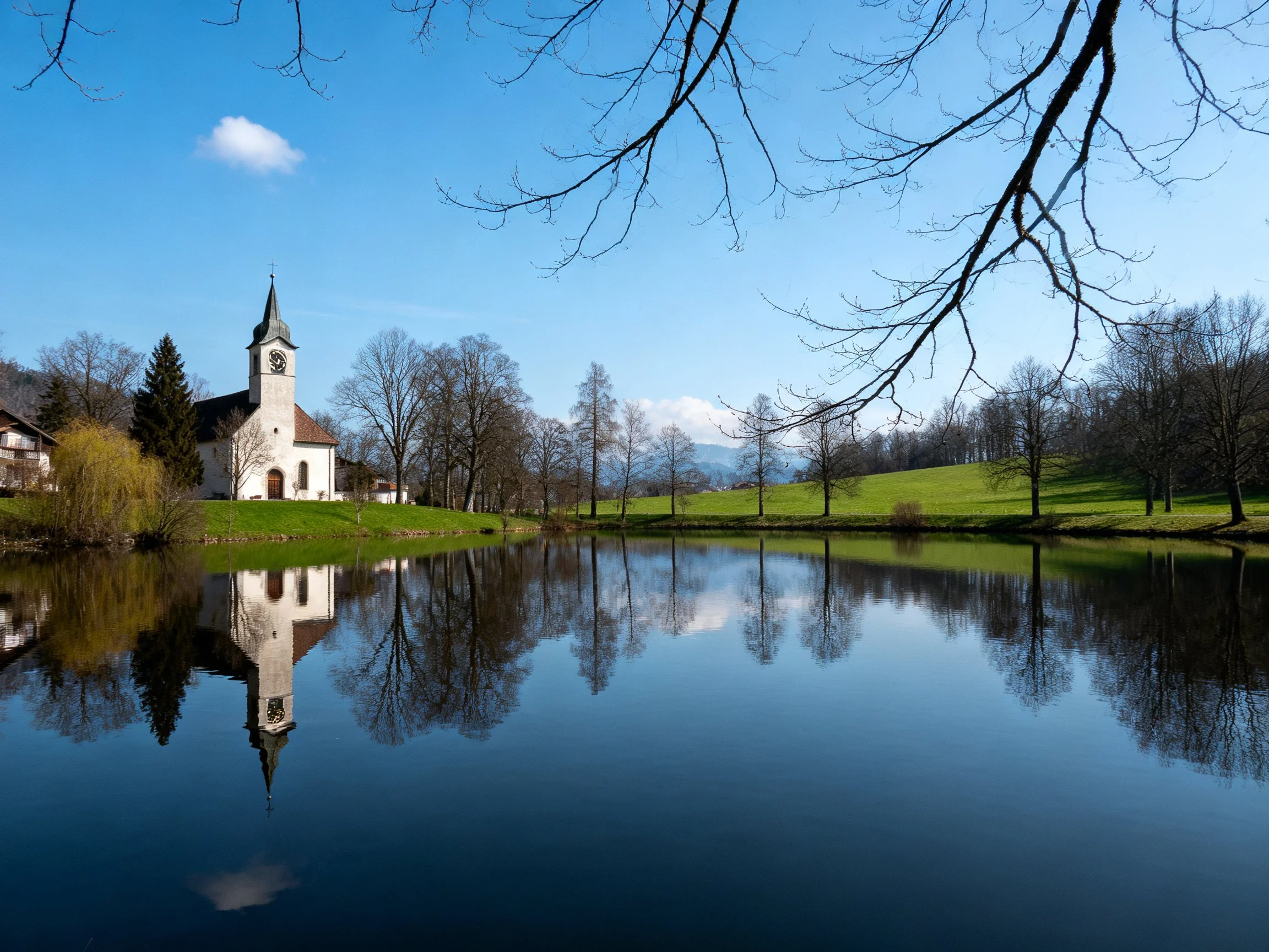 A white church with clock tower beside a reflective lake