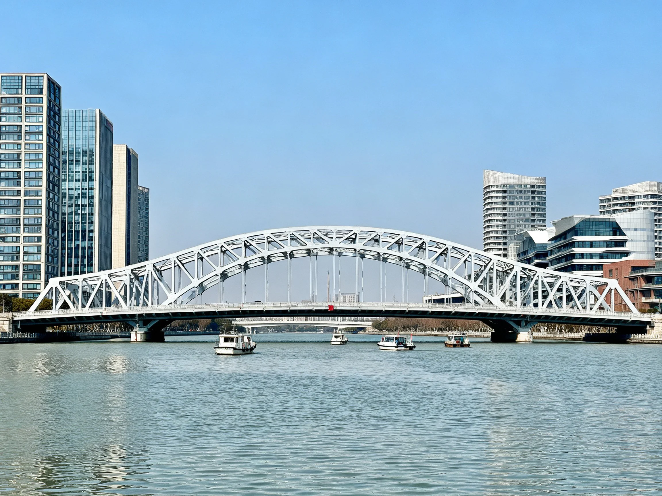 A white steel arch bridge spans a calm river near modern skyscrapers