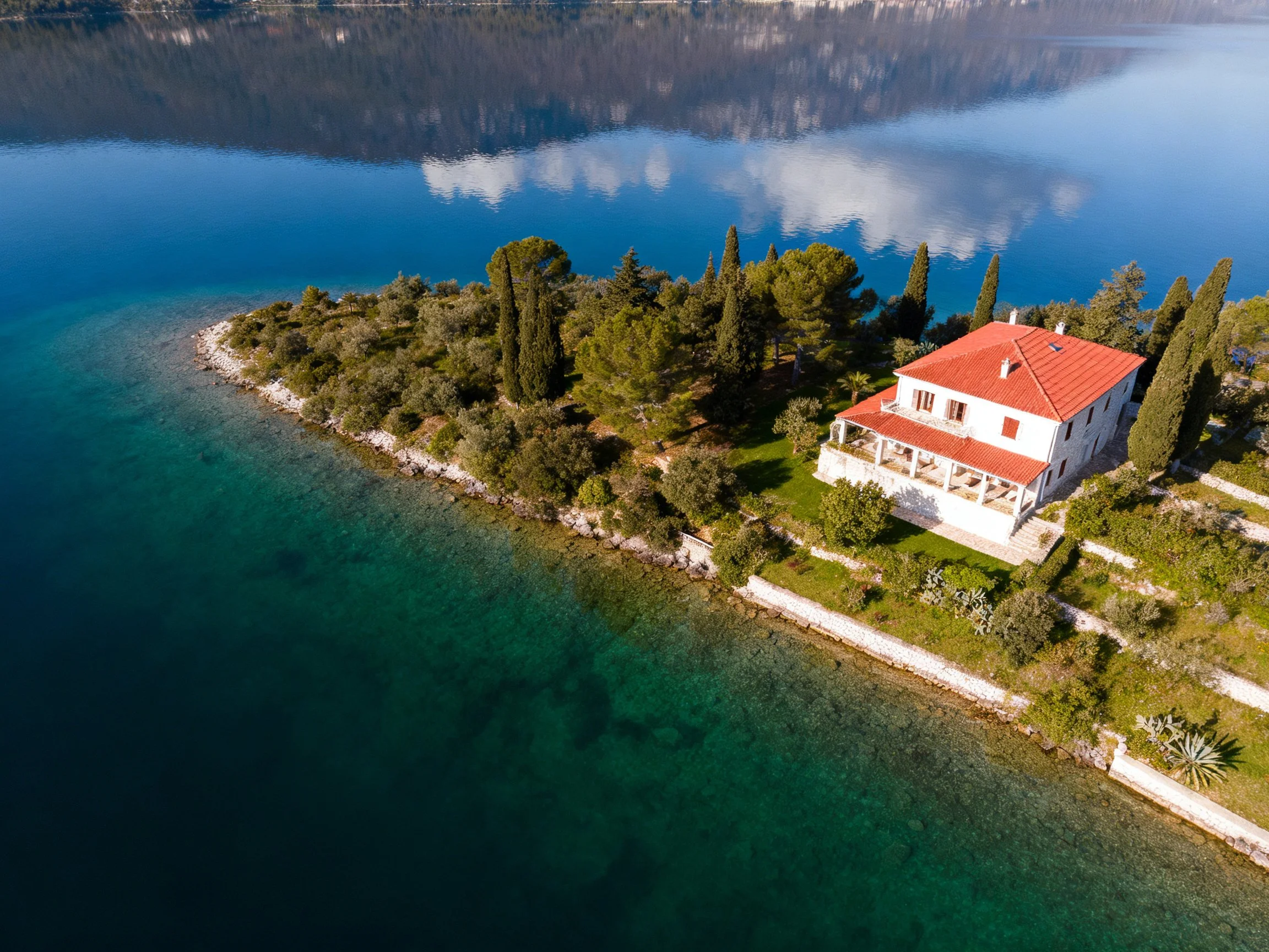 A white two - story house with red roof on a lush coastal island