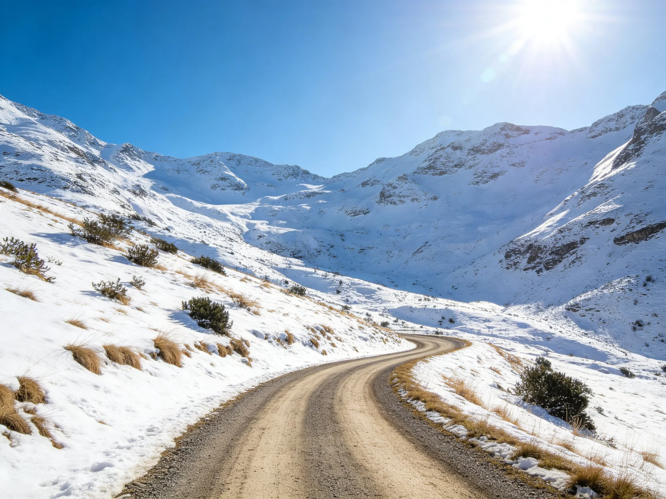 A winding dirt road cuts through snow-covered mountain slopes