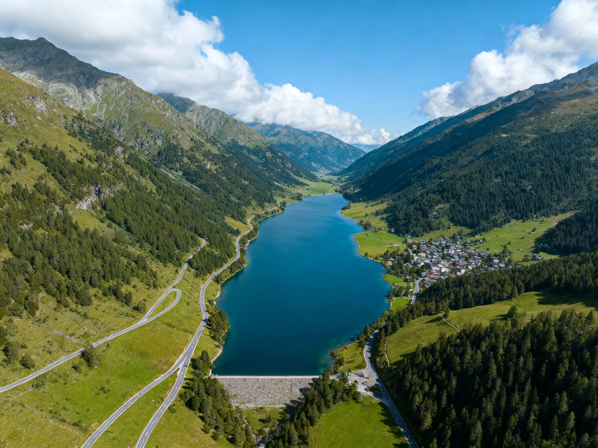 Alpine valley with deep blue lake, forested slopes, and winding roads