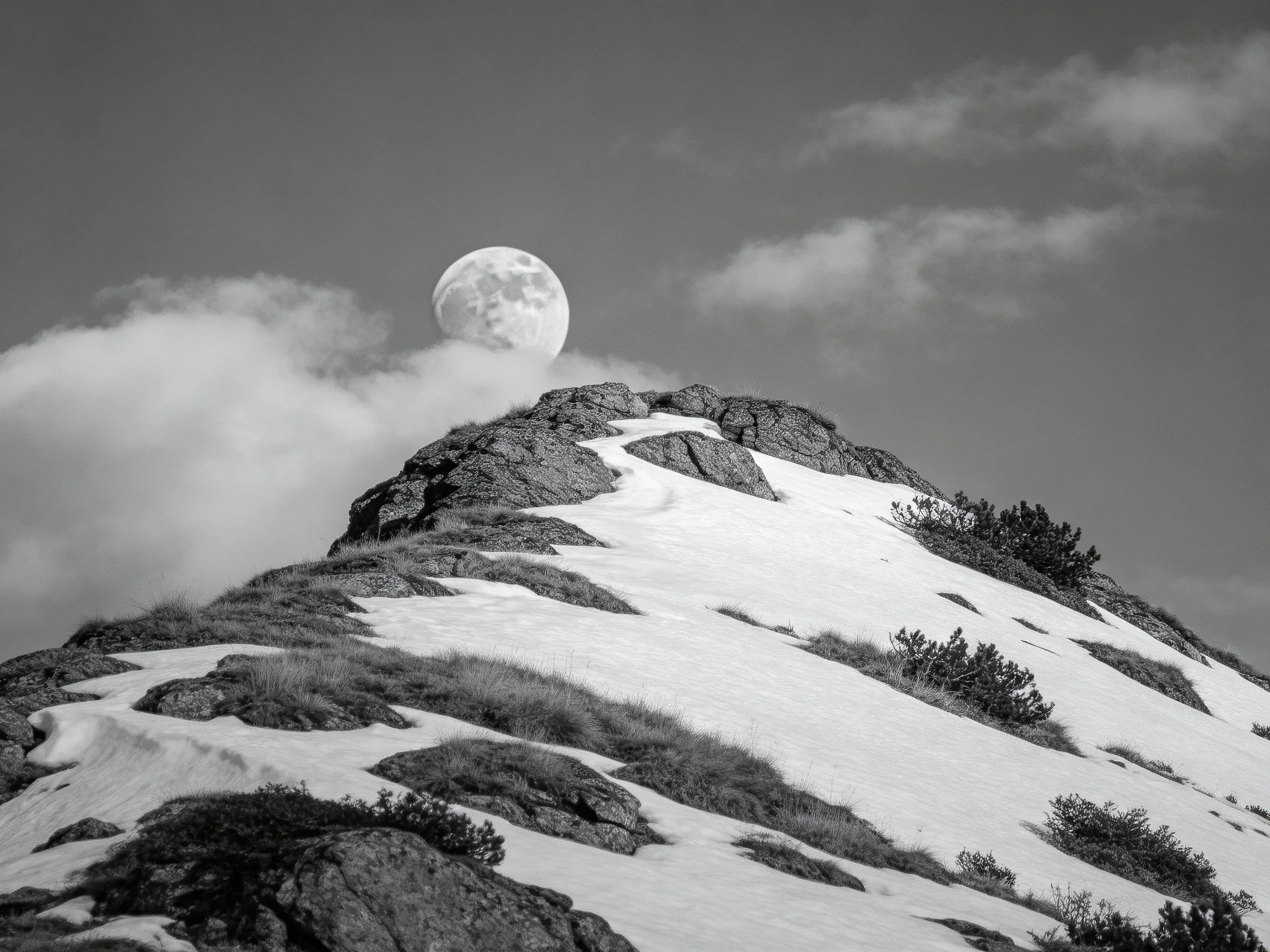 Black and white snowy mountain peak with large moon and clouds