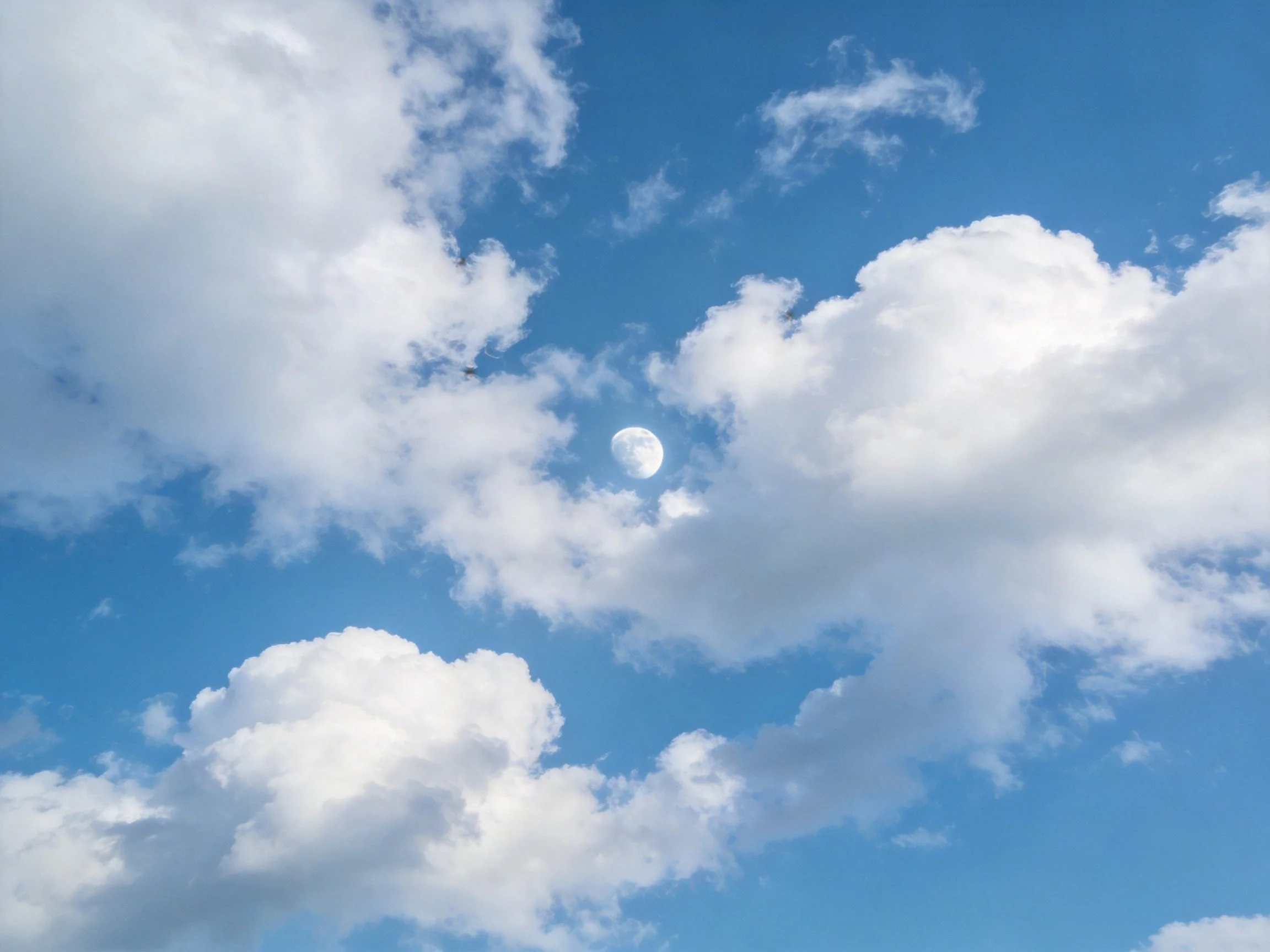 Bright blue sky with fluffy white clouds and a visible moon