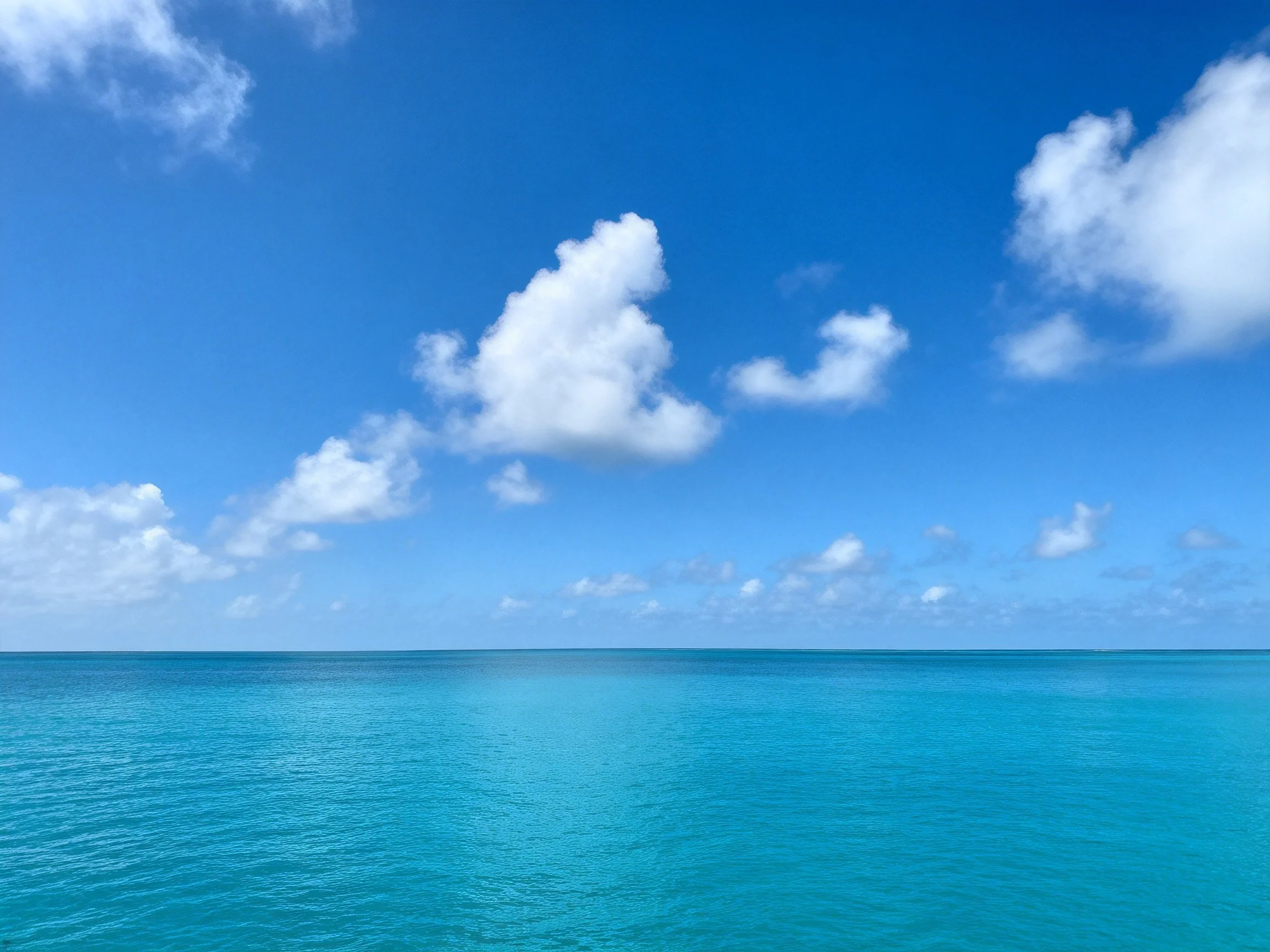 Bright blue sky with scattered white clouds over calm turquoise water
