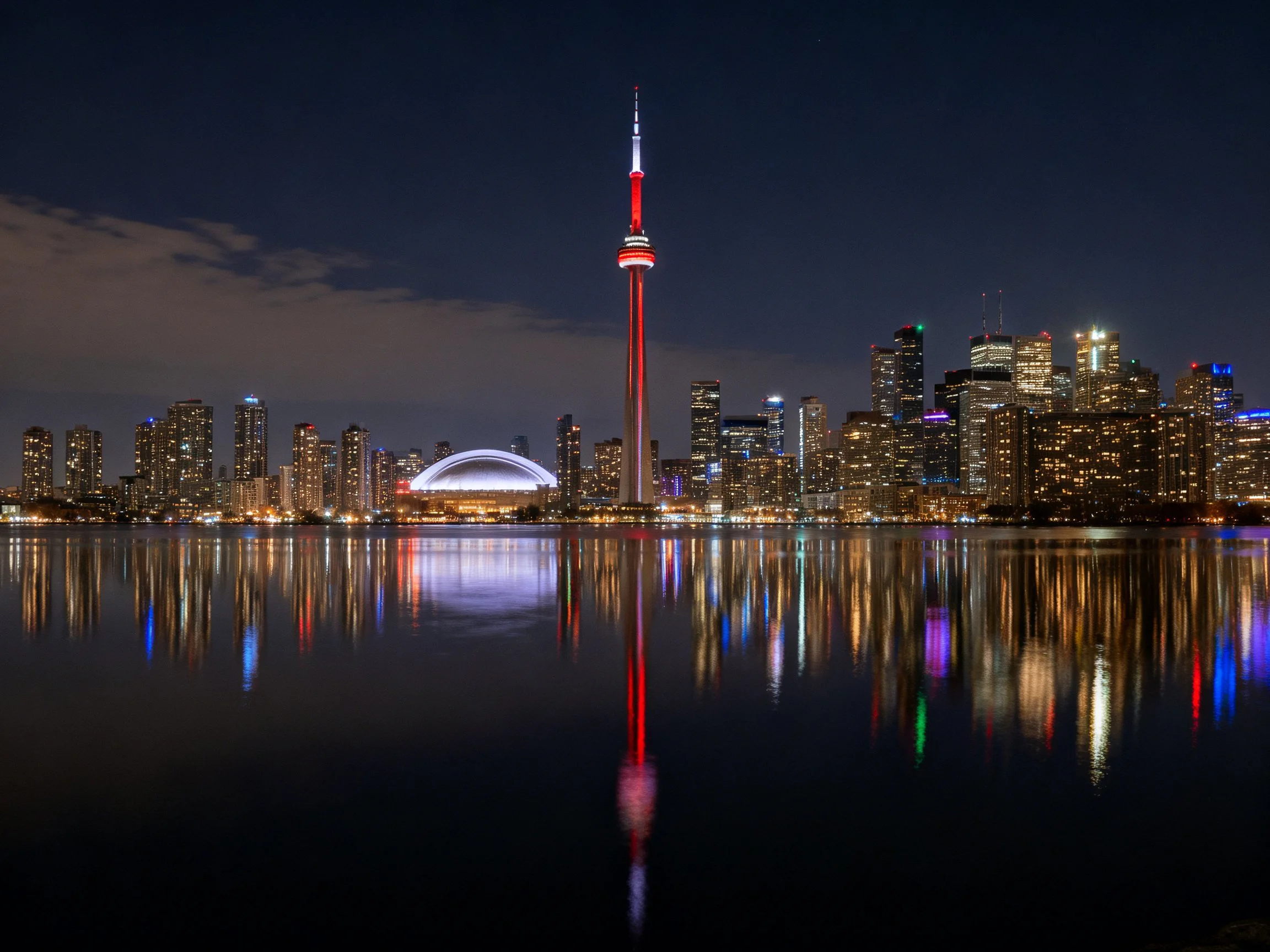 Brightly lit city skyline with red tower reflected in calm water