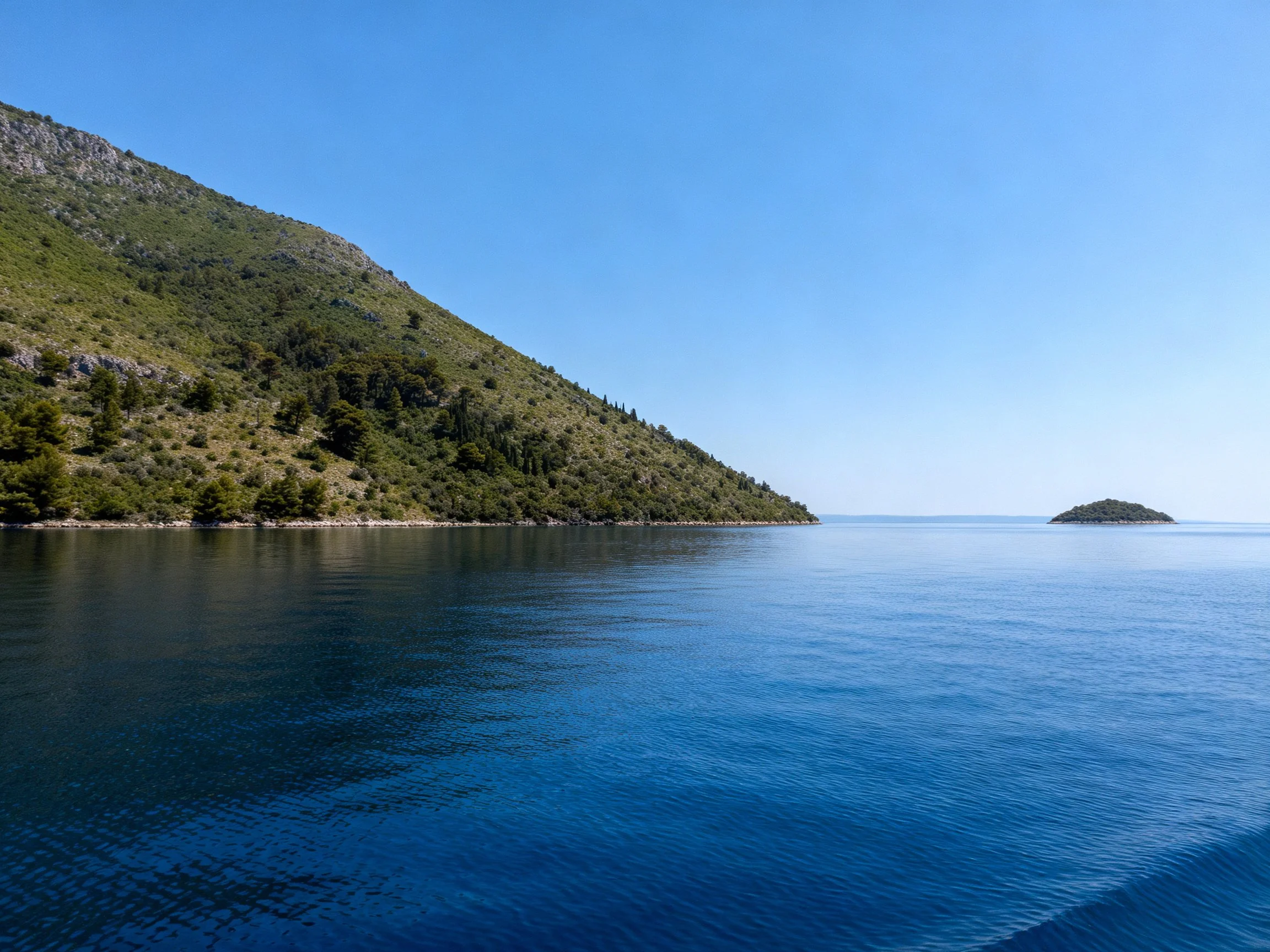 Calm blue waters beside a lush green hill with a small island
