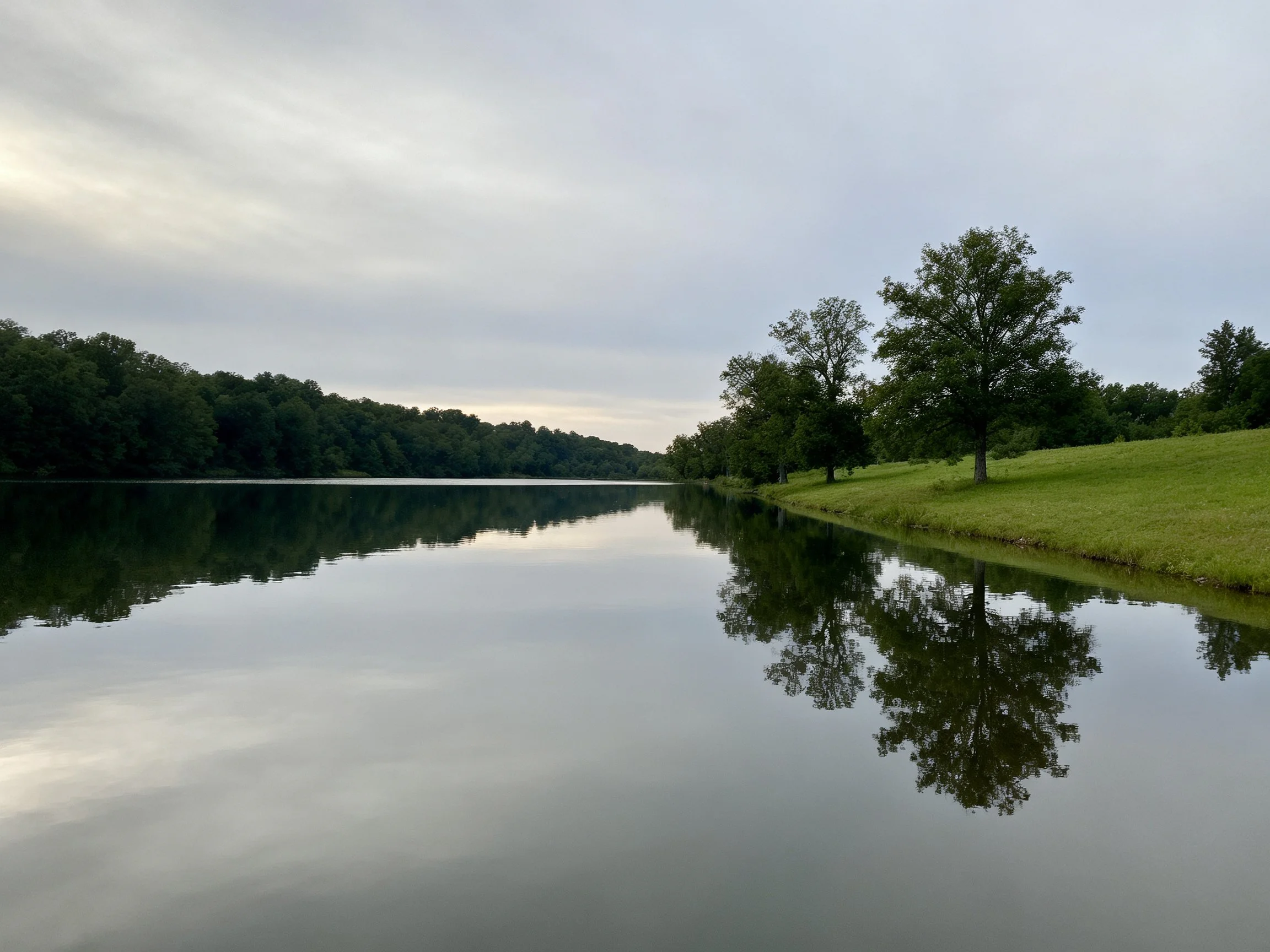 Calm lake reflects lush trees and overcast sky