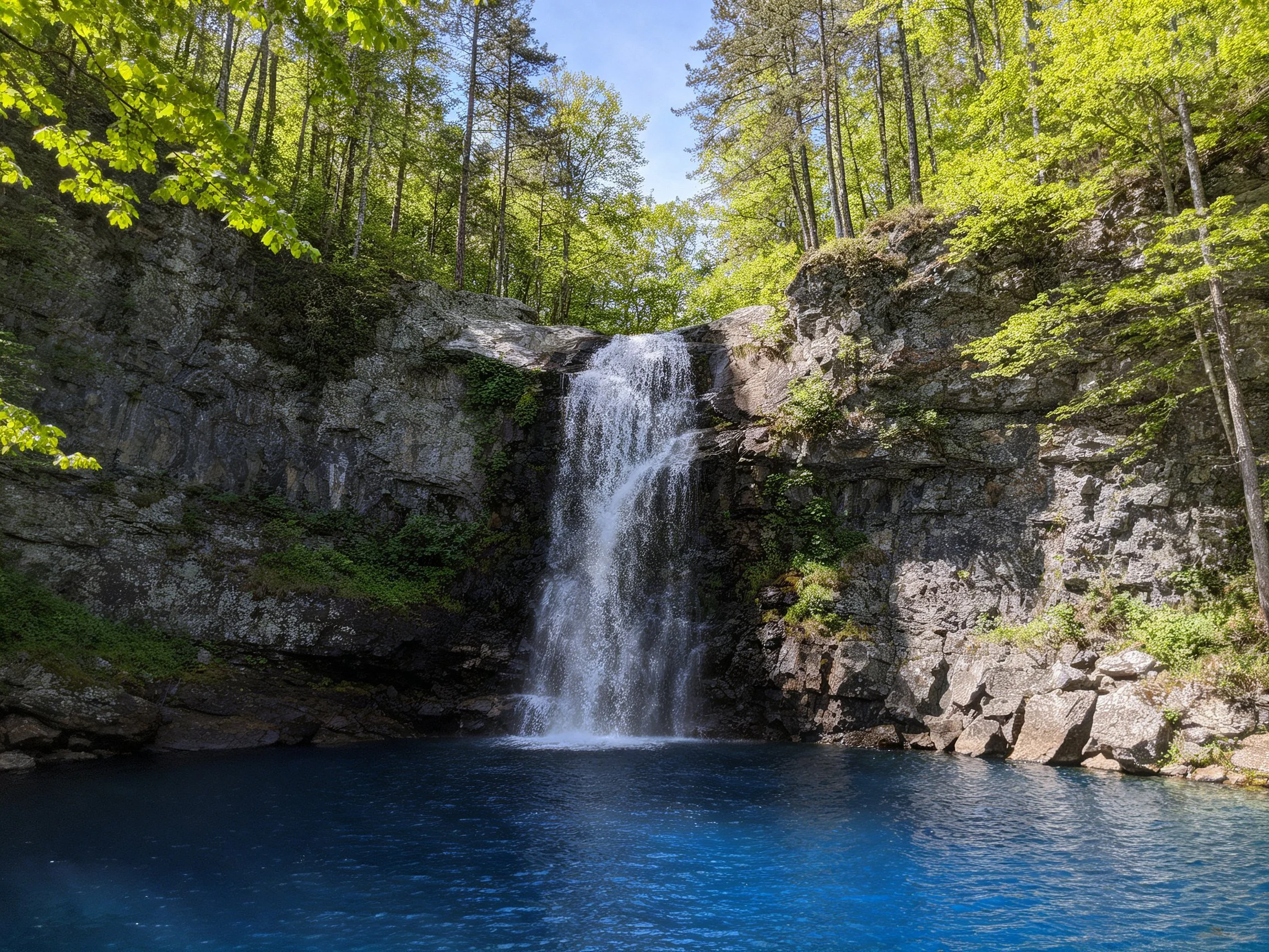 Cascading waterfall into blue pool between rocky cliffs and green forest