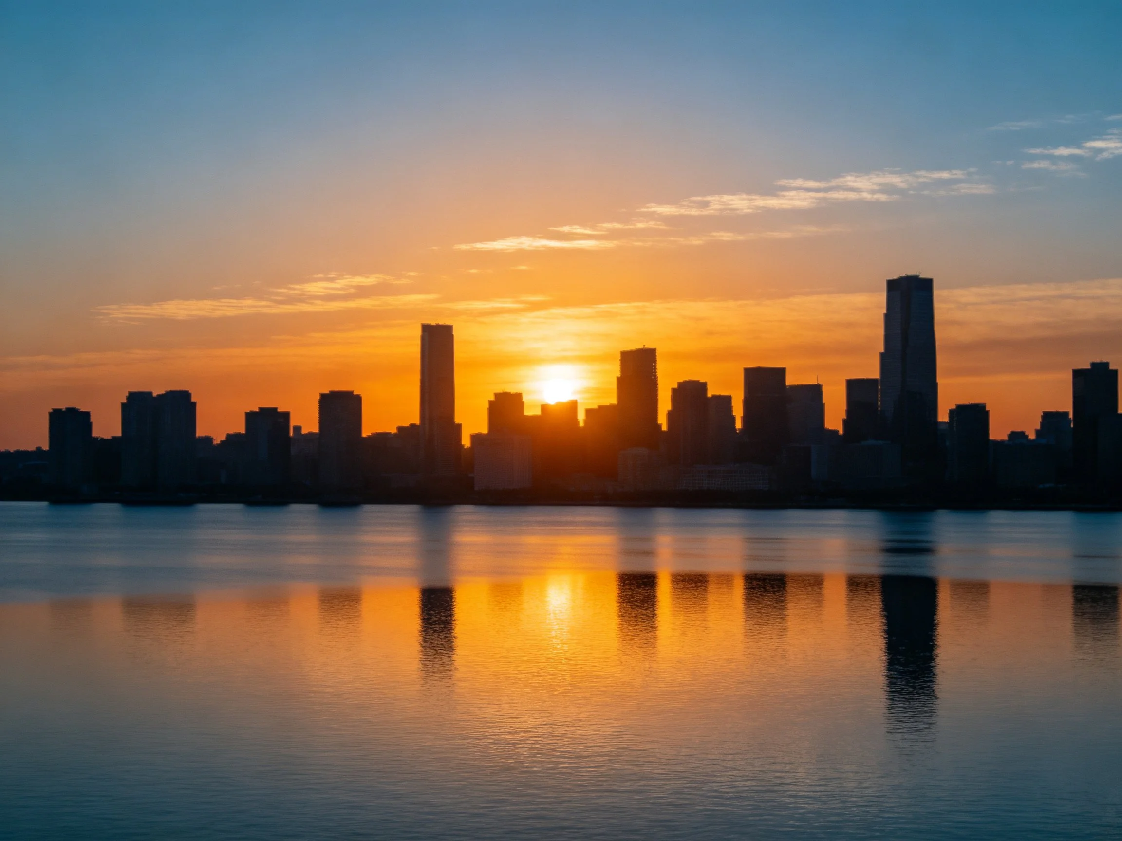 City skyline silhouetted by vibrant sunset over calm water