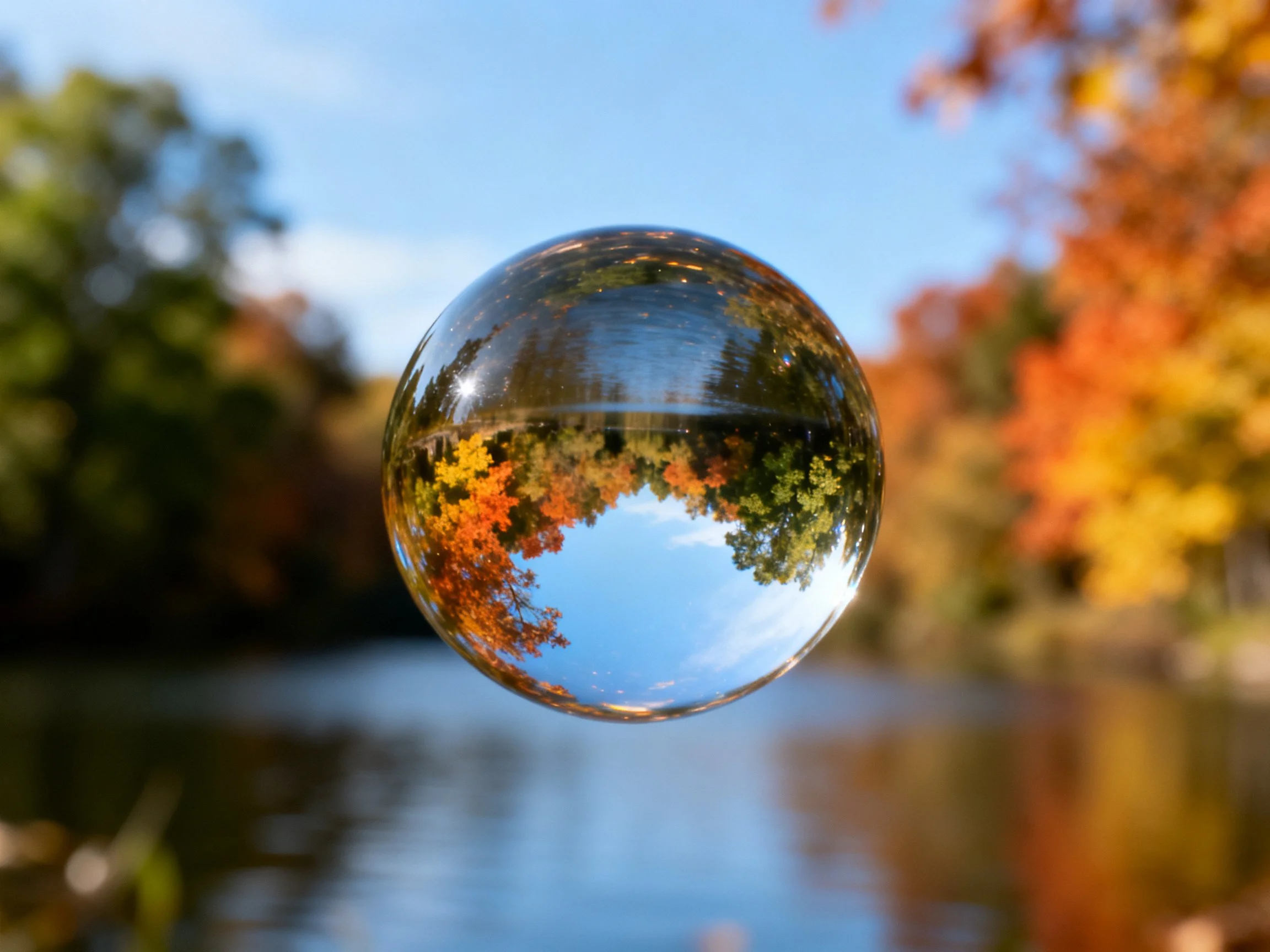 Clear glass sphere reflects colorful fall scenery over calm water