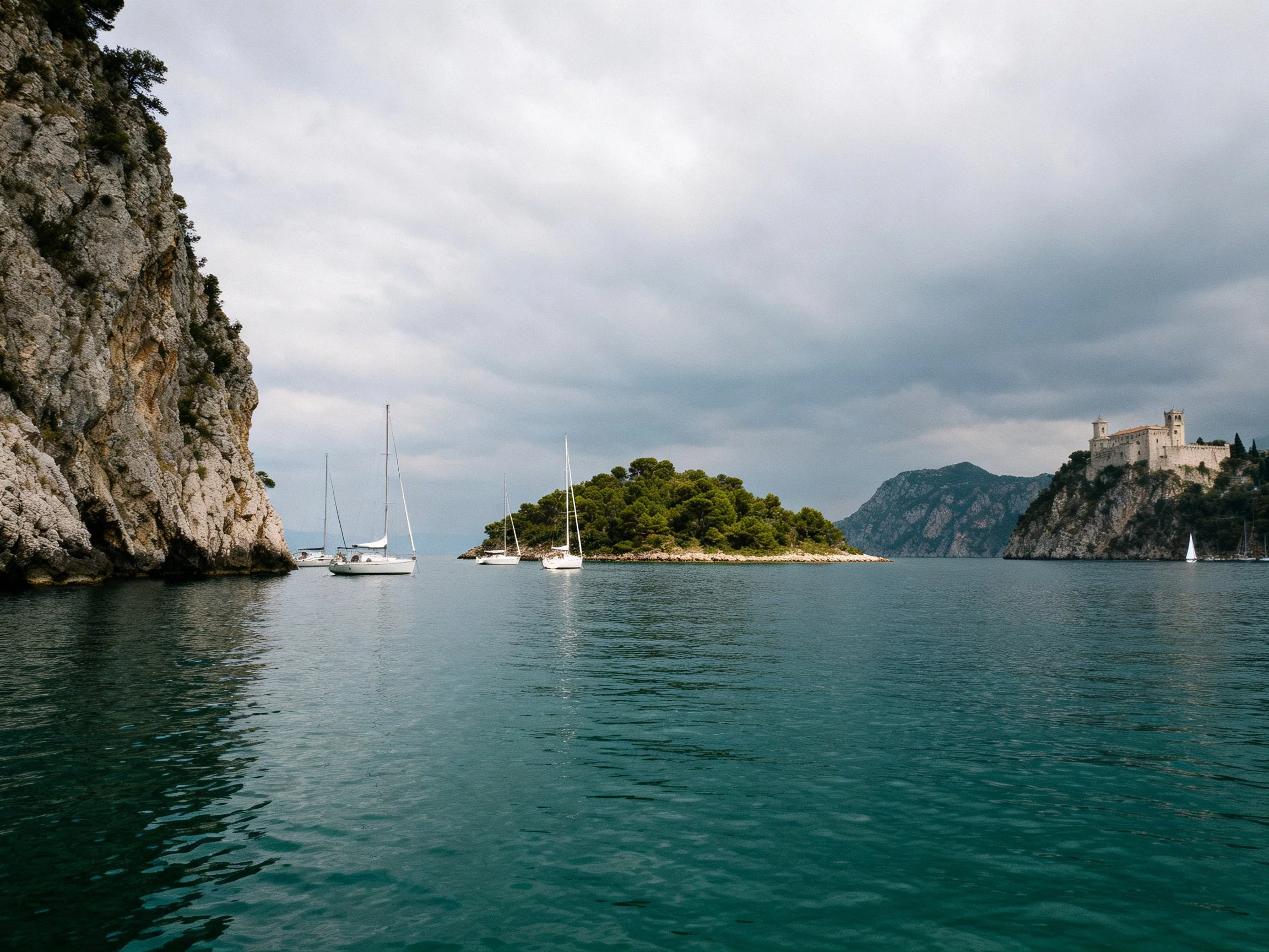 Cliffside Bay with Sailboats, Island, and Castle Under Overcast Sky