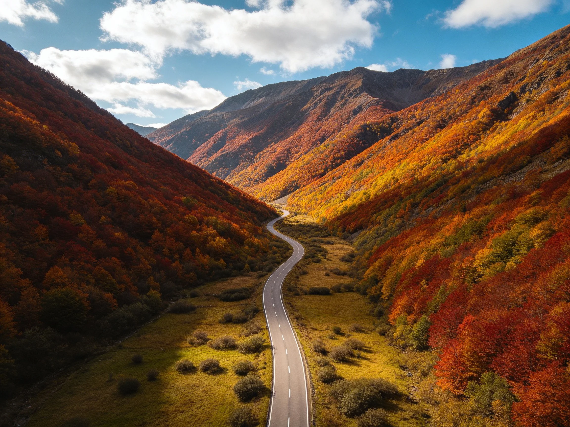 Colorful autumn mountains surround a winding valley road.