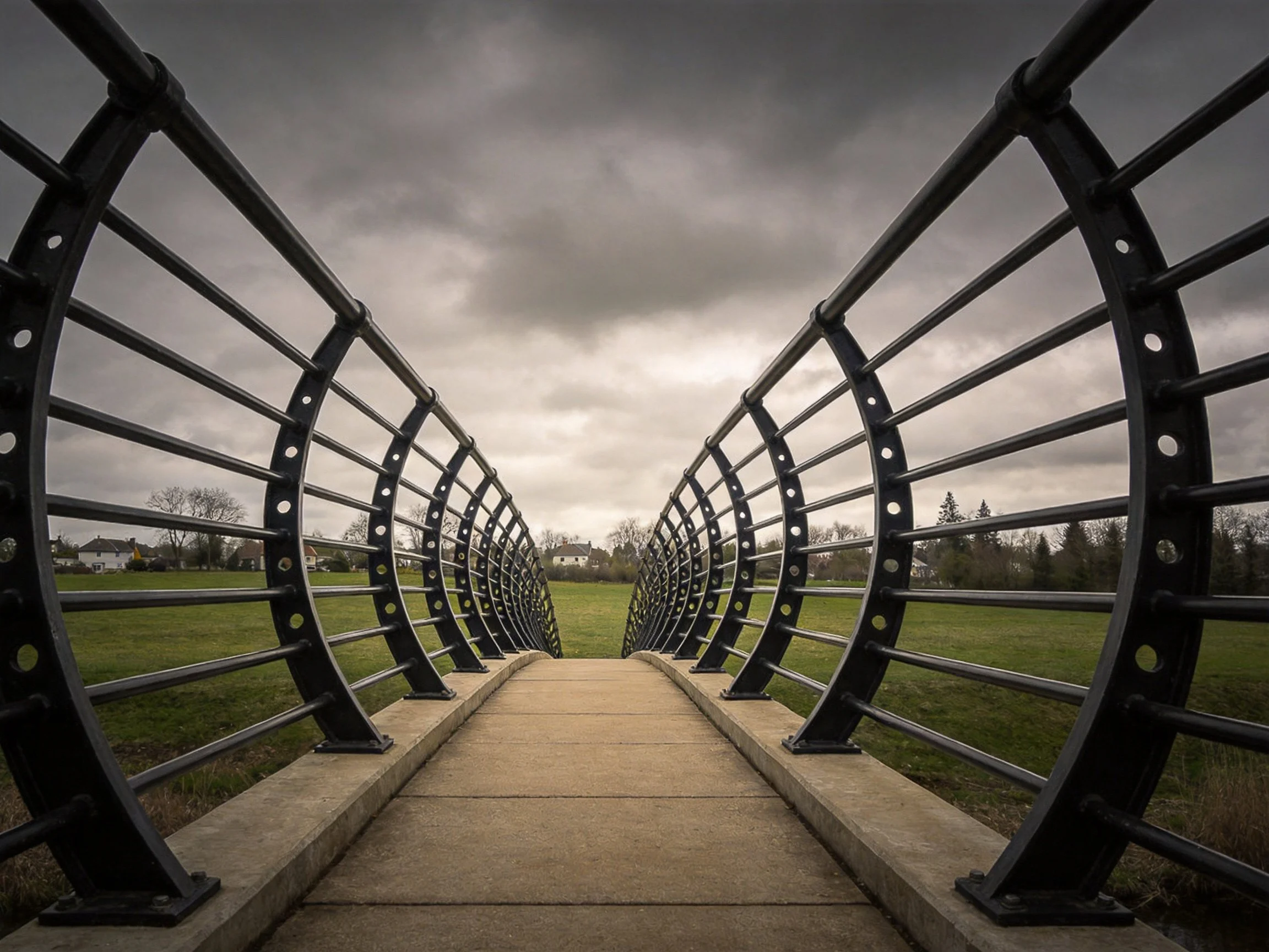 Curved Metal Bridge Tunneling Through Grassy Field Under Overcast Sky