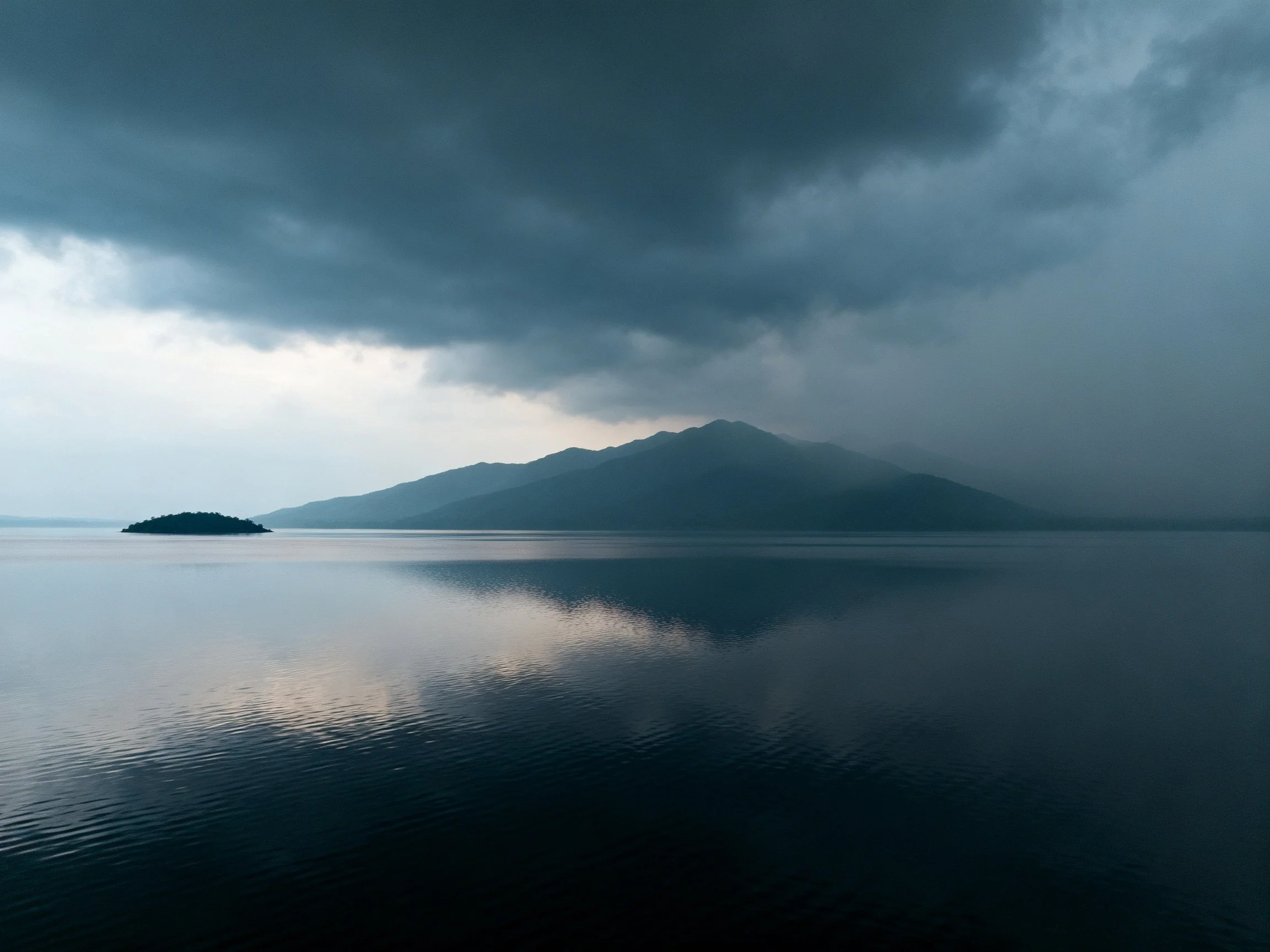 Dark storm clouds loom over a mountain lake with a small island